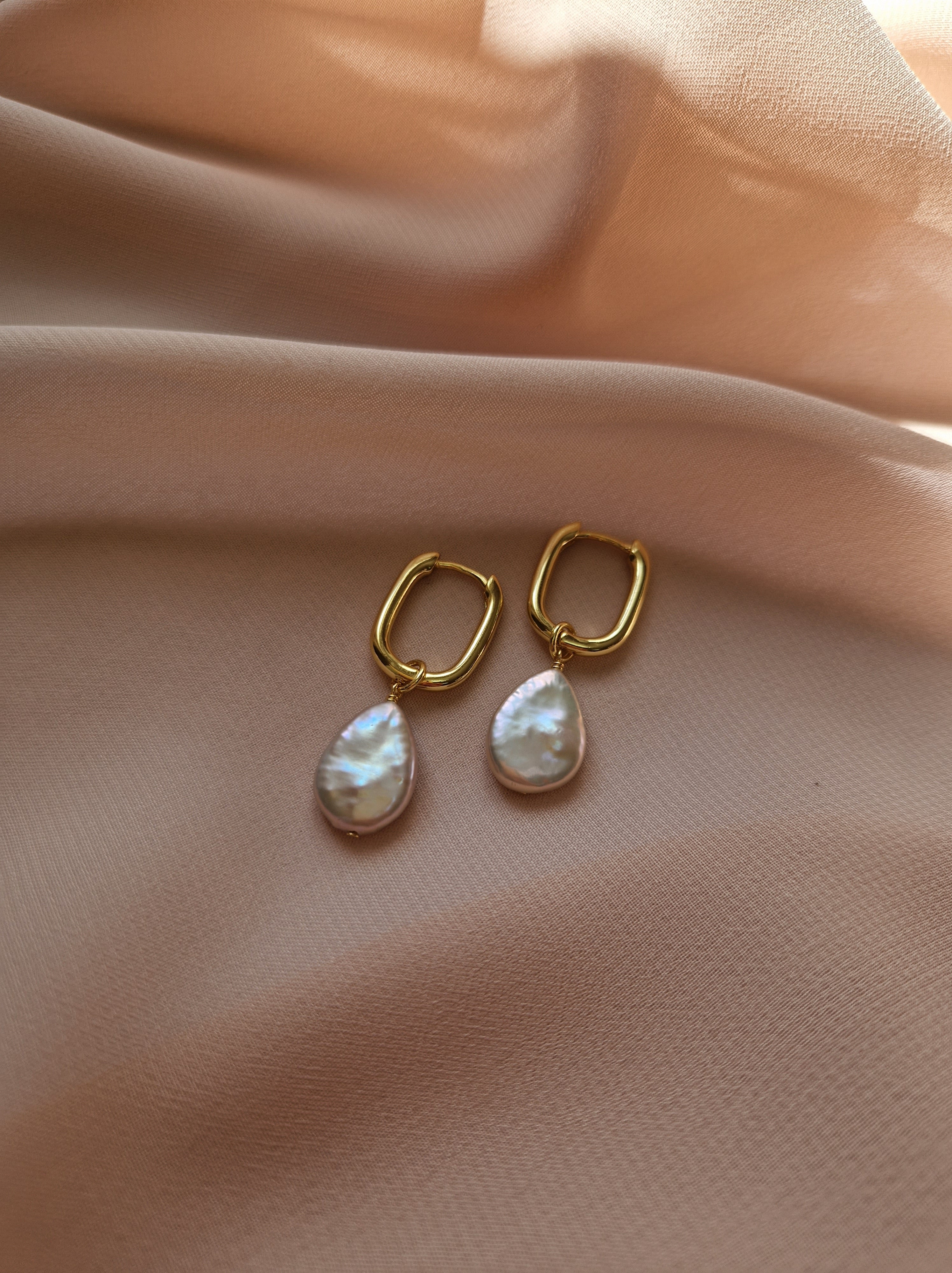 Gold-plated earrings with pearl drops on a soft pink fabric background