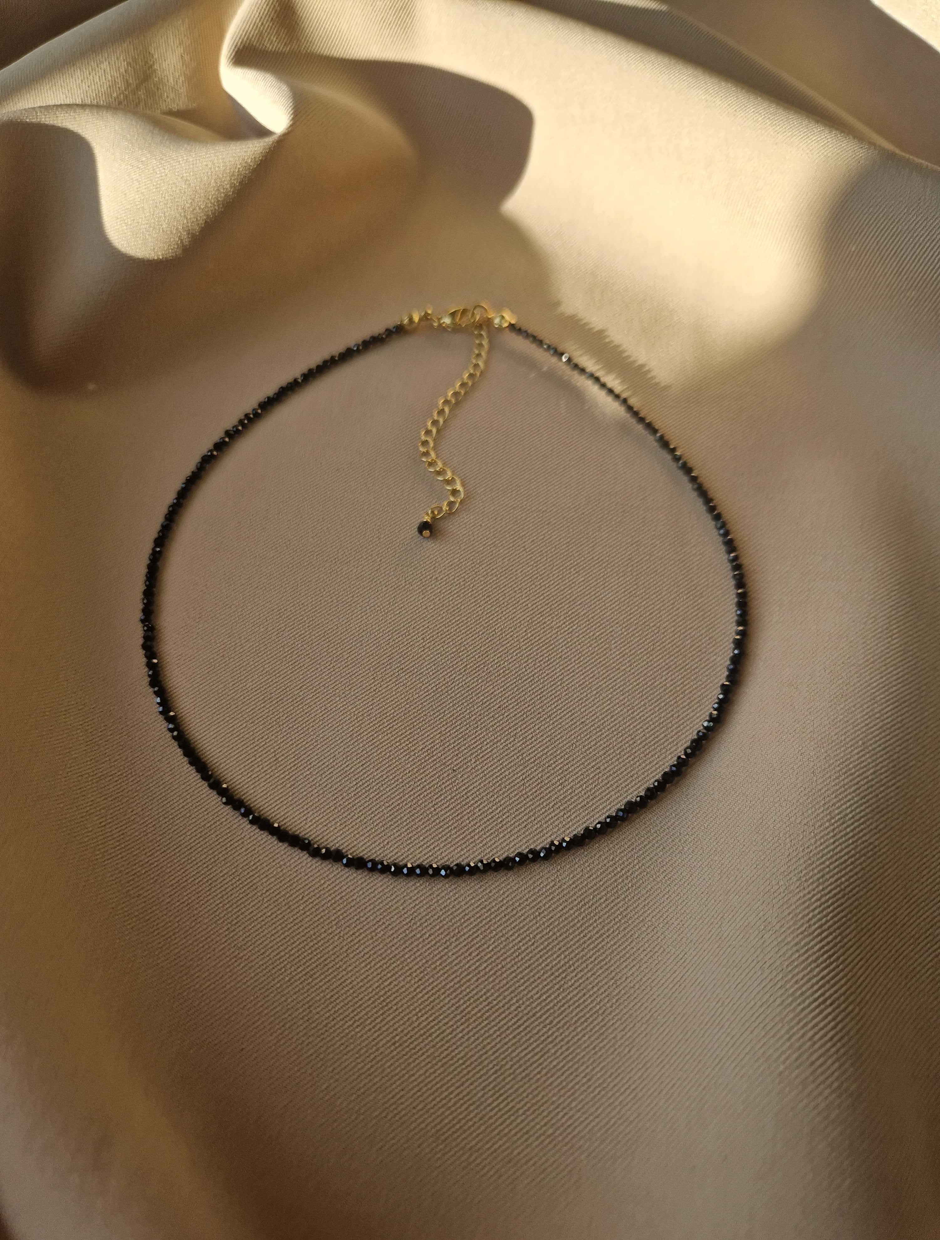 Black spinel beaded necklace on a beige fabric background