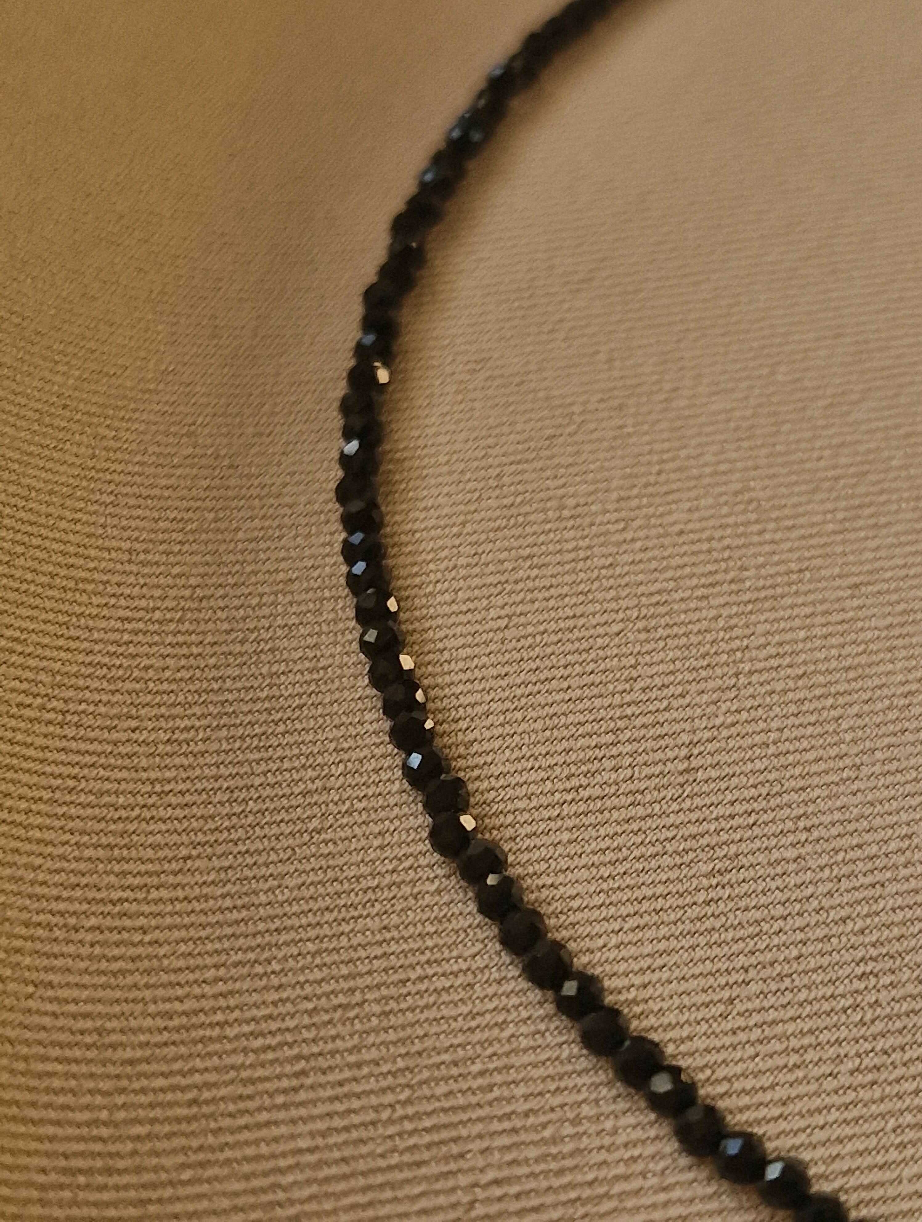 Black spinel beaded necklace on a beige fabric background