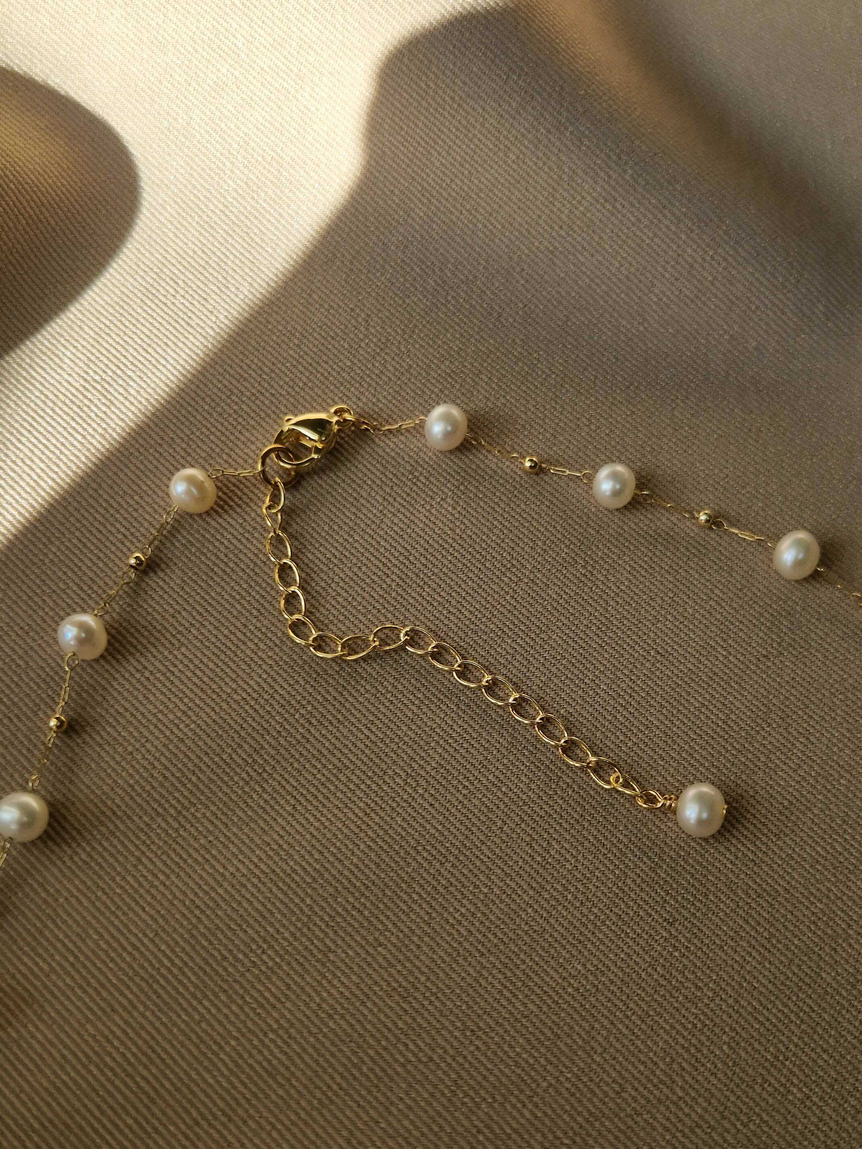 Gold-plated chain necklace with pearls on a textured surface