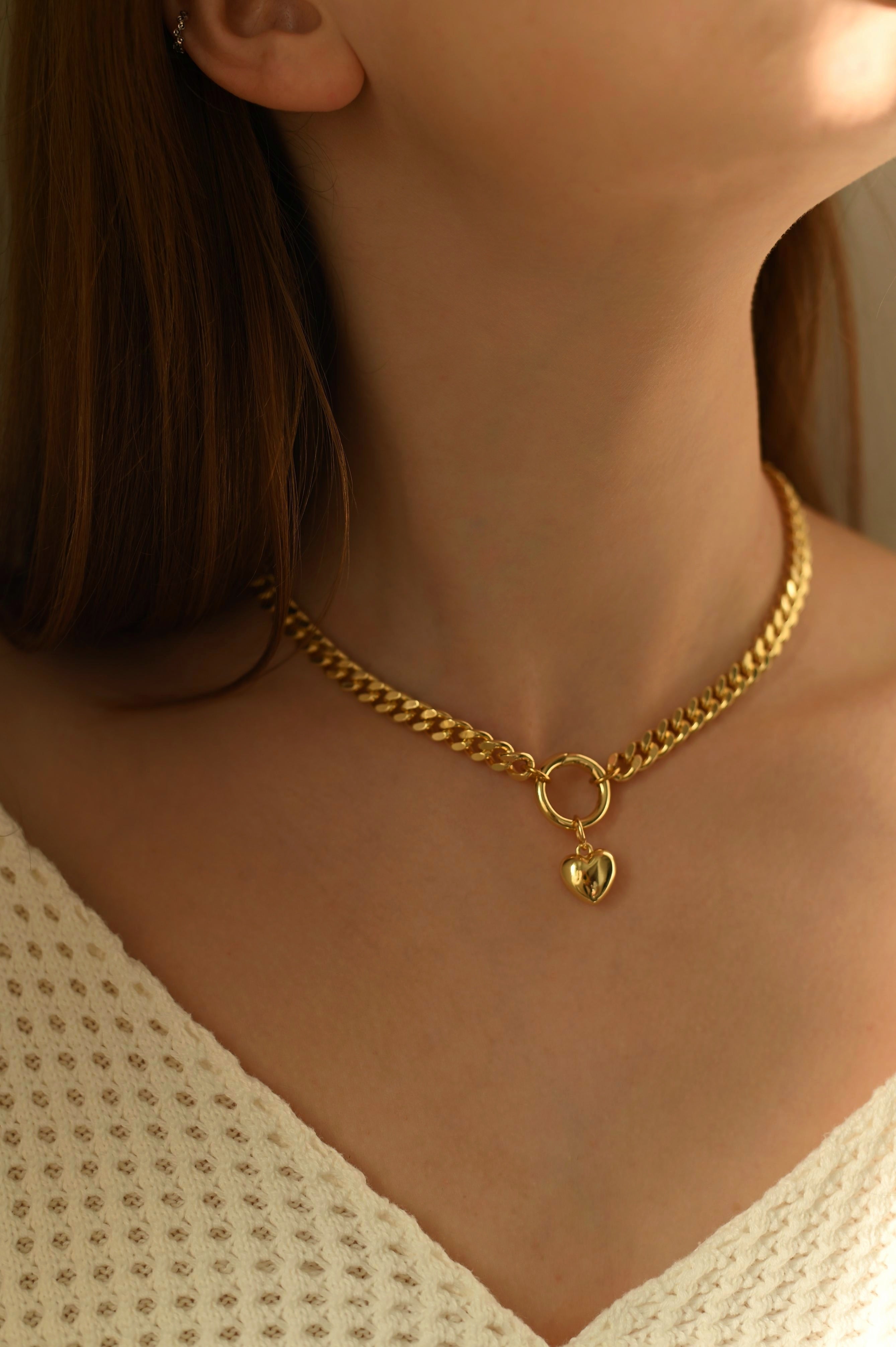 Gold-plated chain necklace with a heart pendant worn by a person