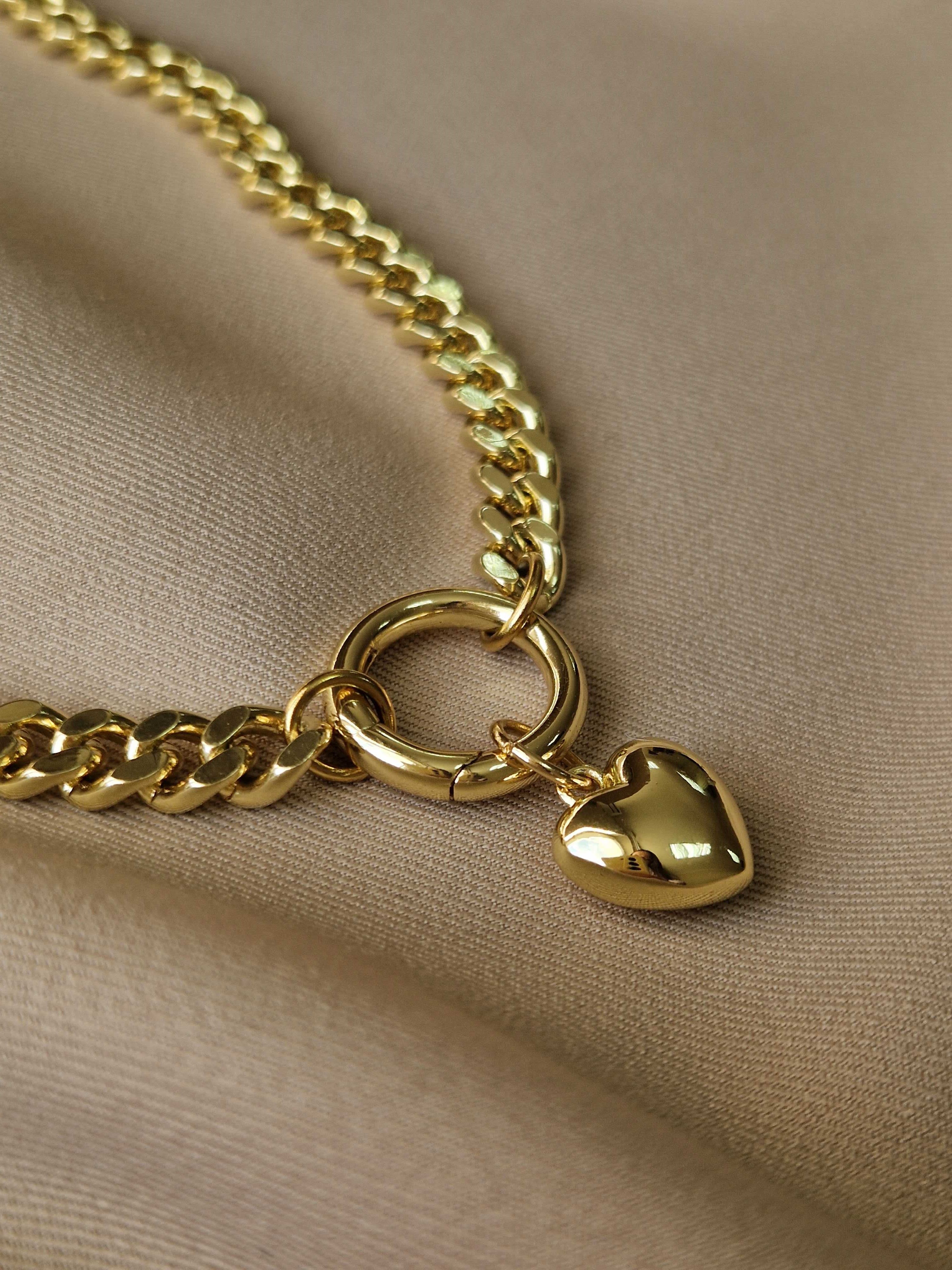 Gold-plated chain necklace with a heart-shaped pendant on a beige fabric background