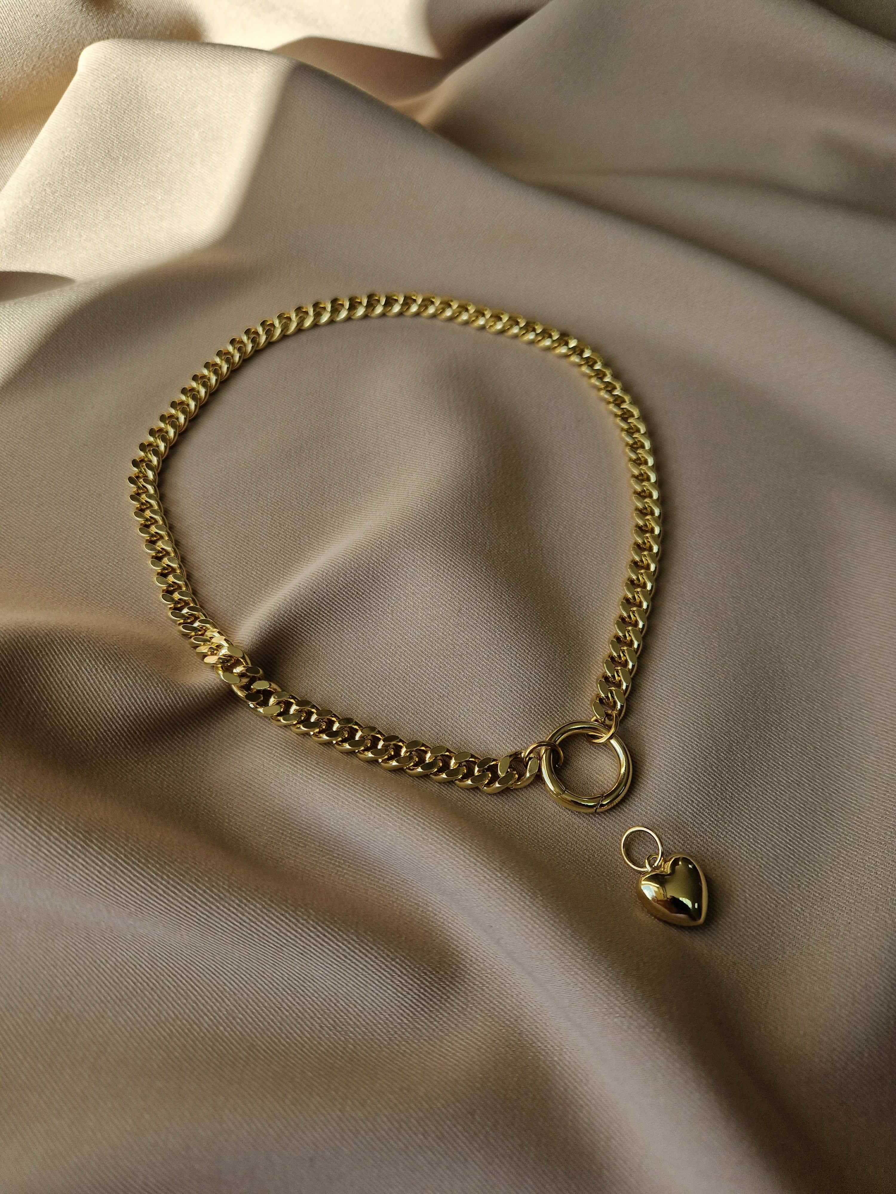 Gold-plated chain bracelet with a heart-shaped charm on a beige fabric background