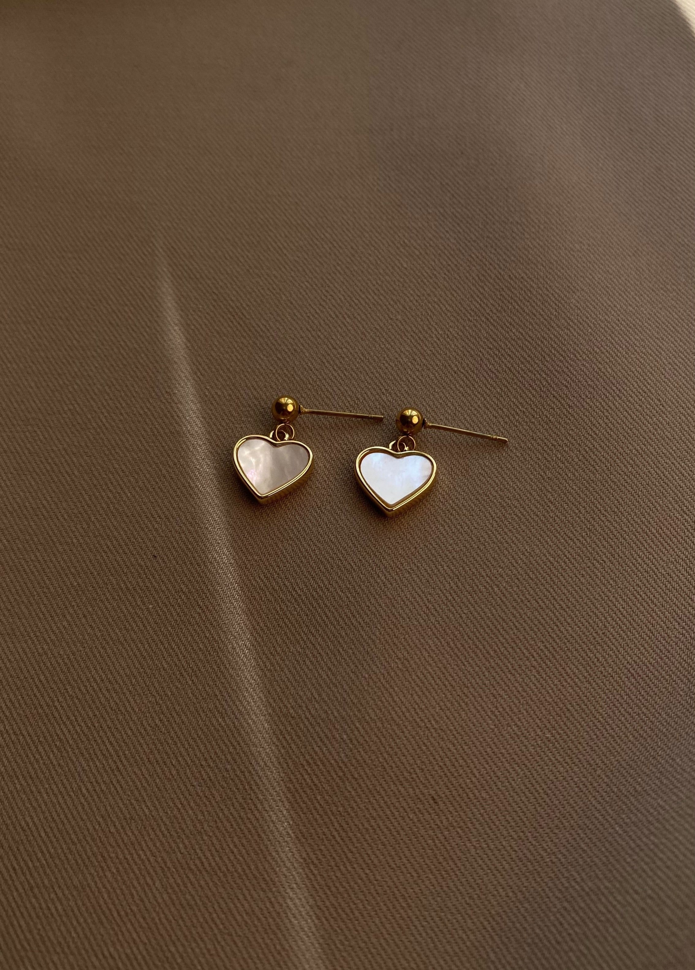 Delicate stud earrings with mother-of-pearl heart charms, offering a romantic and feminine touch with minimalist design and soft shimmer.
