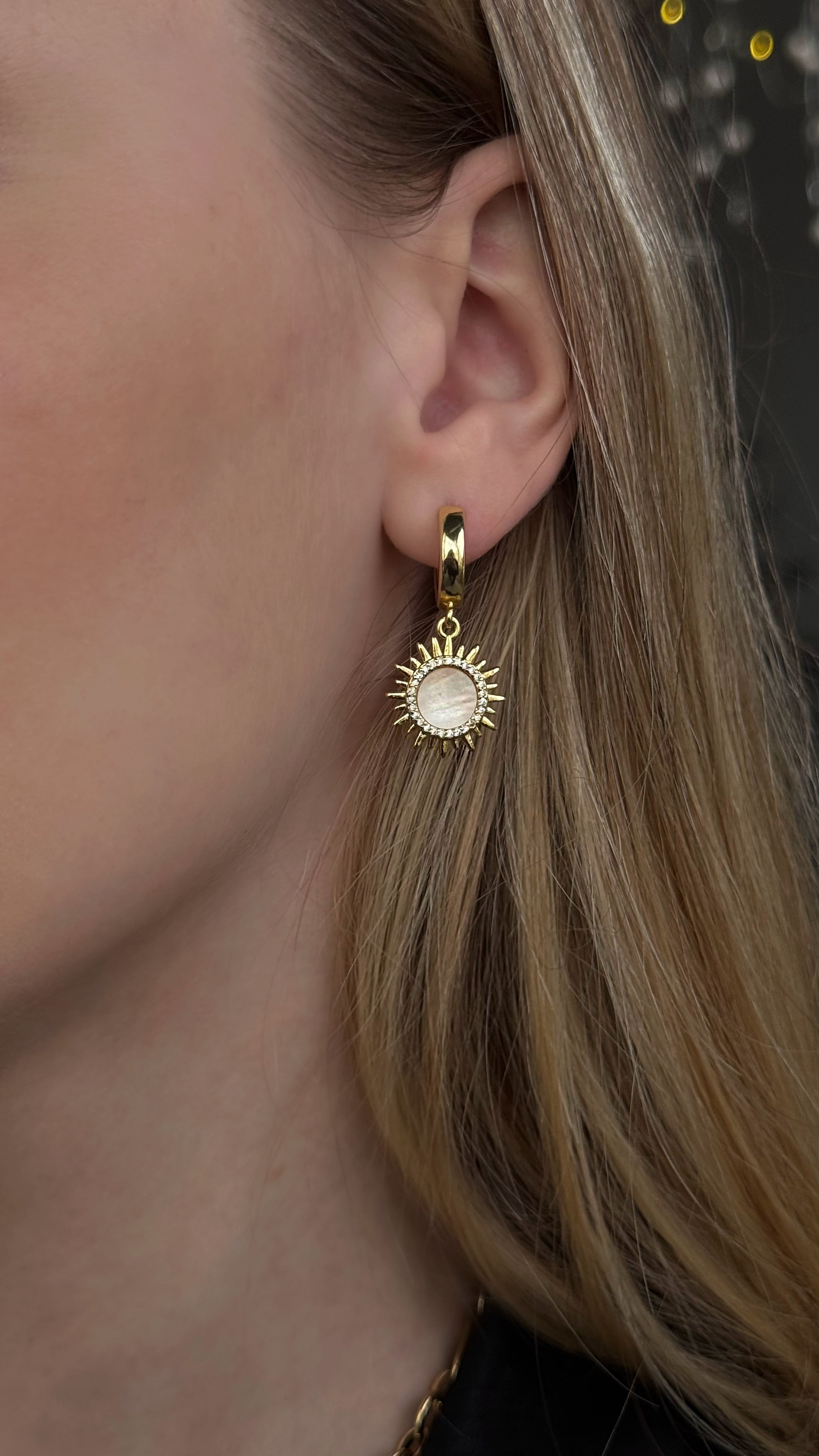 Close-up of 18k gold plated sun-shaped earrings with mother of pearl inlay – elegant handmade celestial jewelry displayed on a neutral background.