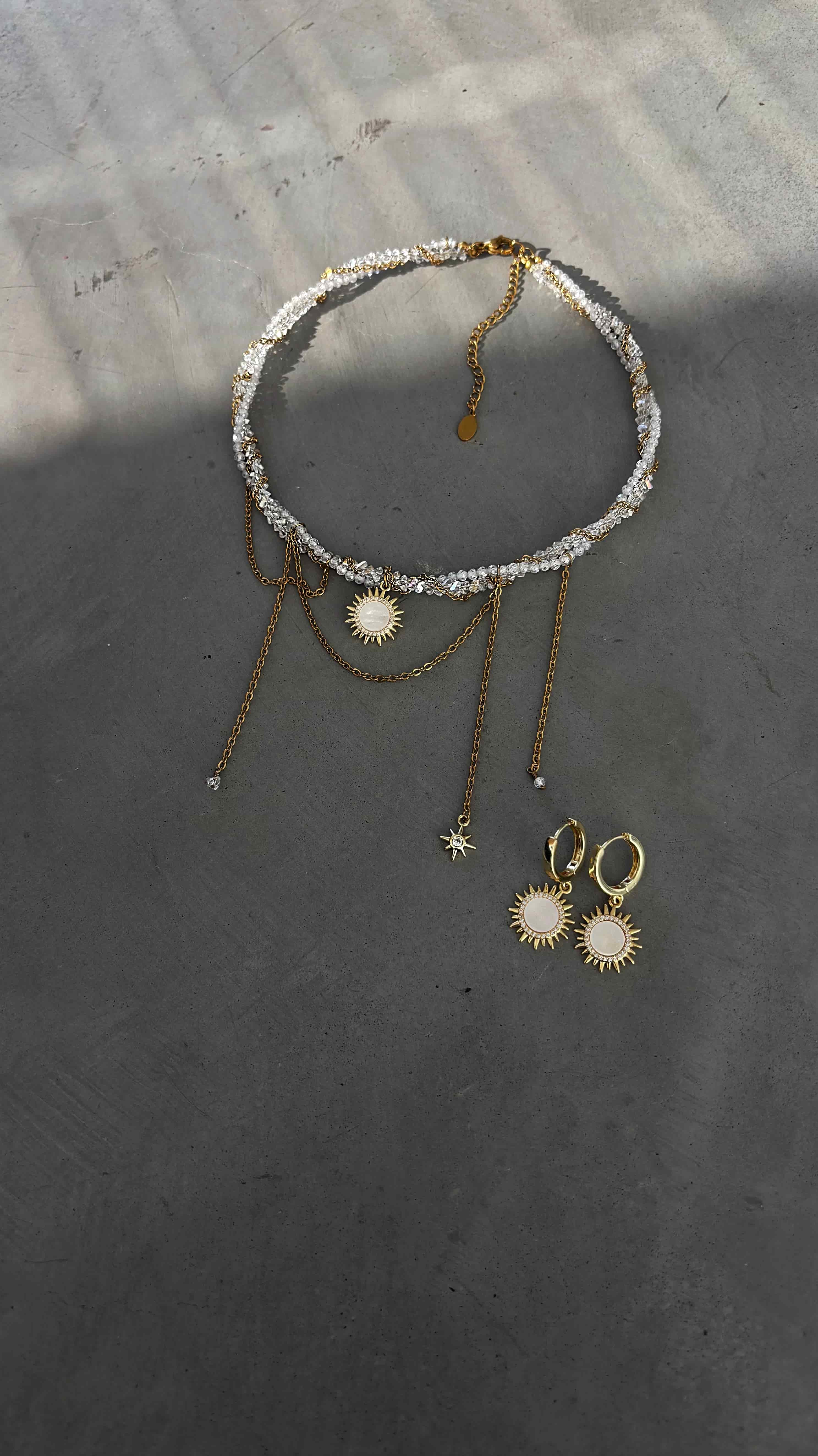 Gold plated sun pendant necklace with twisted chain and matching mother of pearl sunshine earrings displayed on a soft neutral background