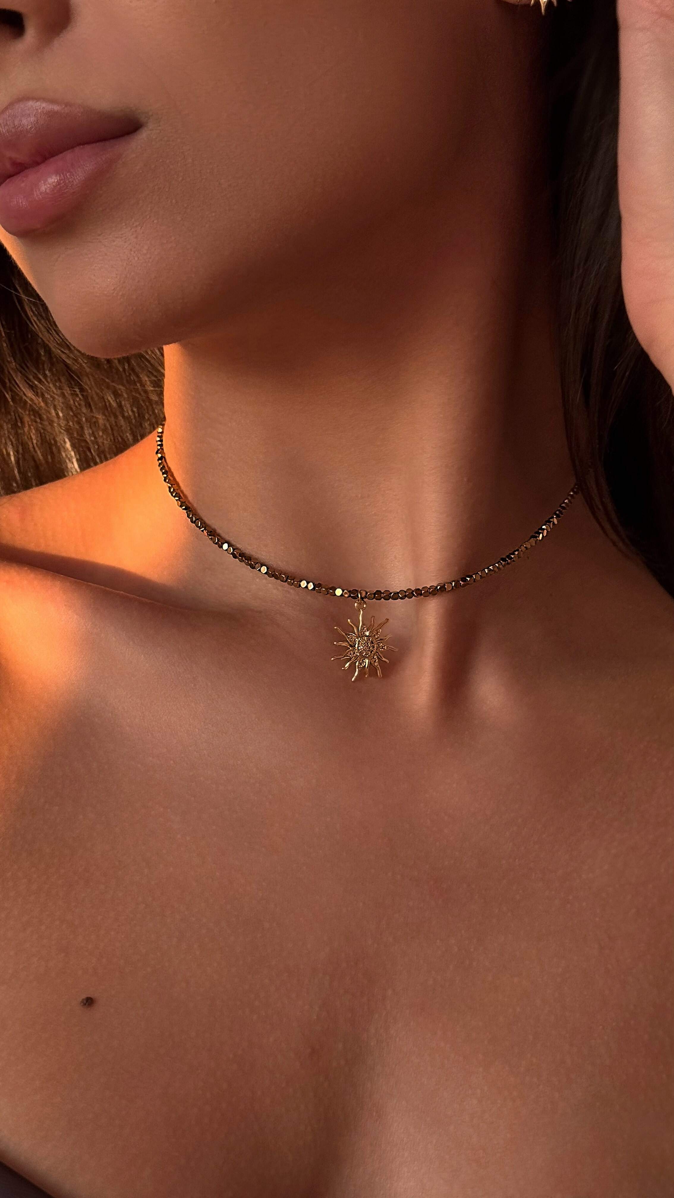 Close-up of a necklace with a sun pendant on a person's neck.