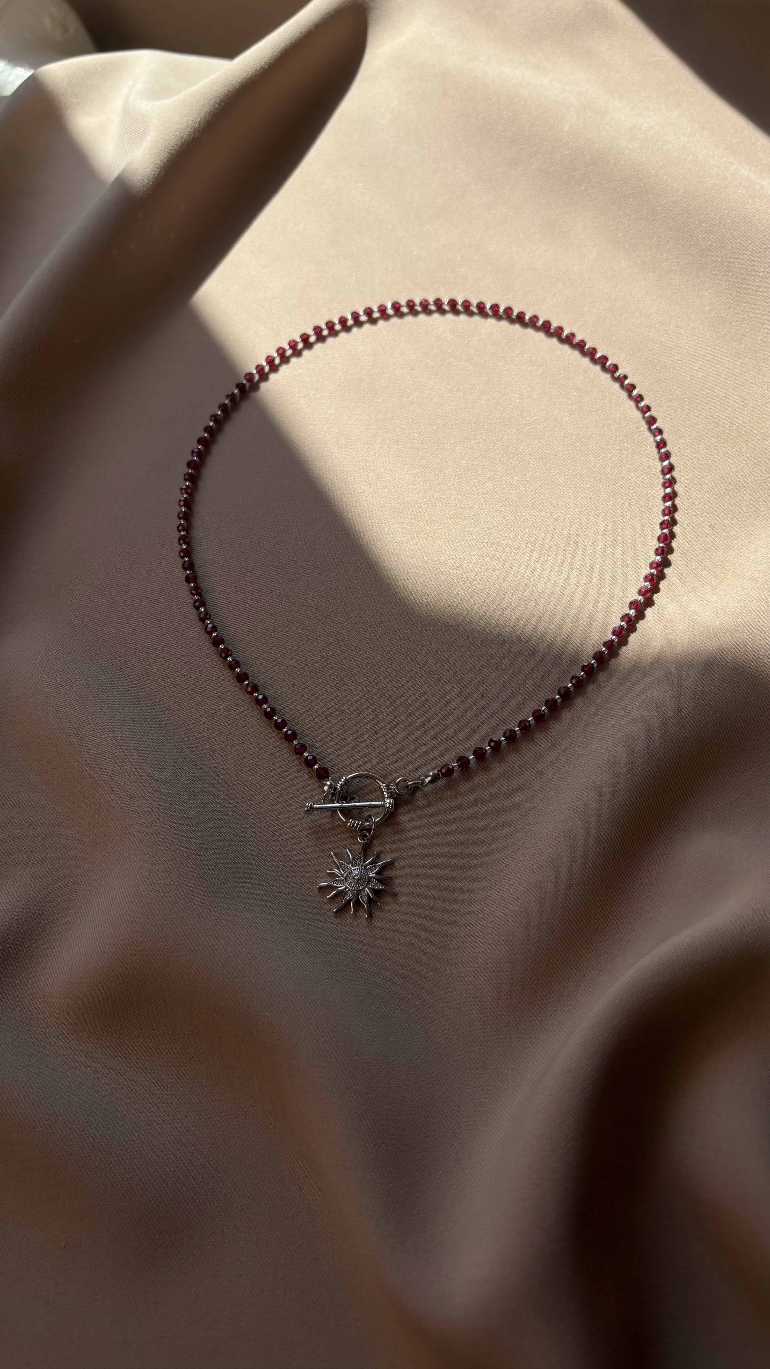 Necklace with red beads of garnet and a sun-shaped pendant on a beige fabric background