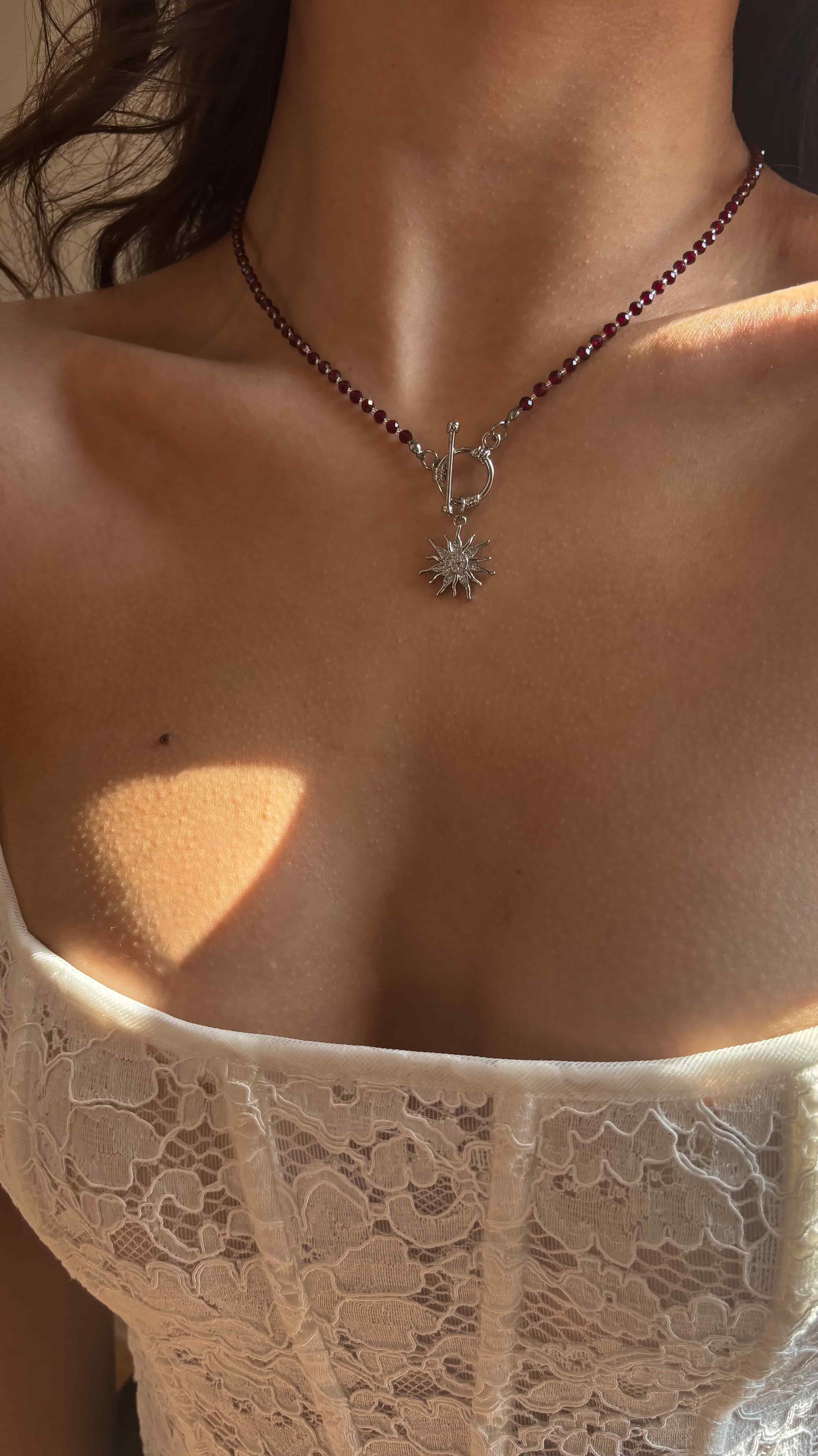 Close-up of a necklace with a sun-pendant on a person wearing a lace garment.