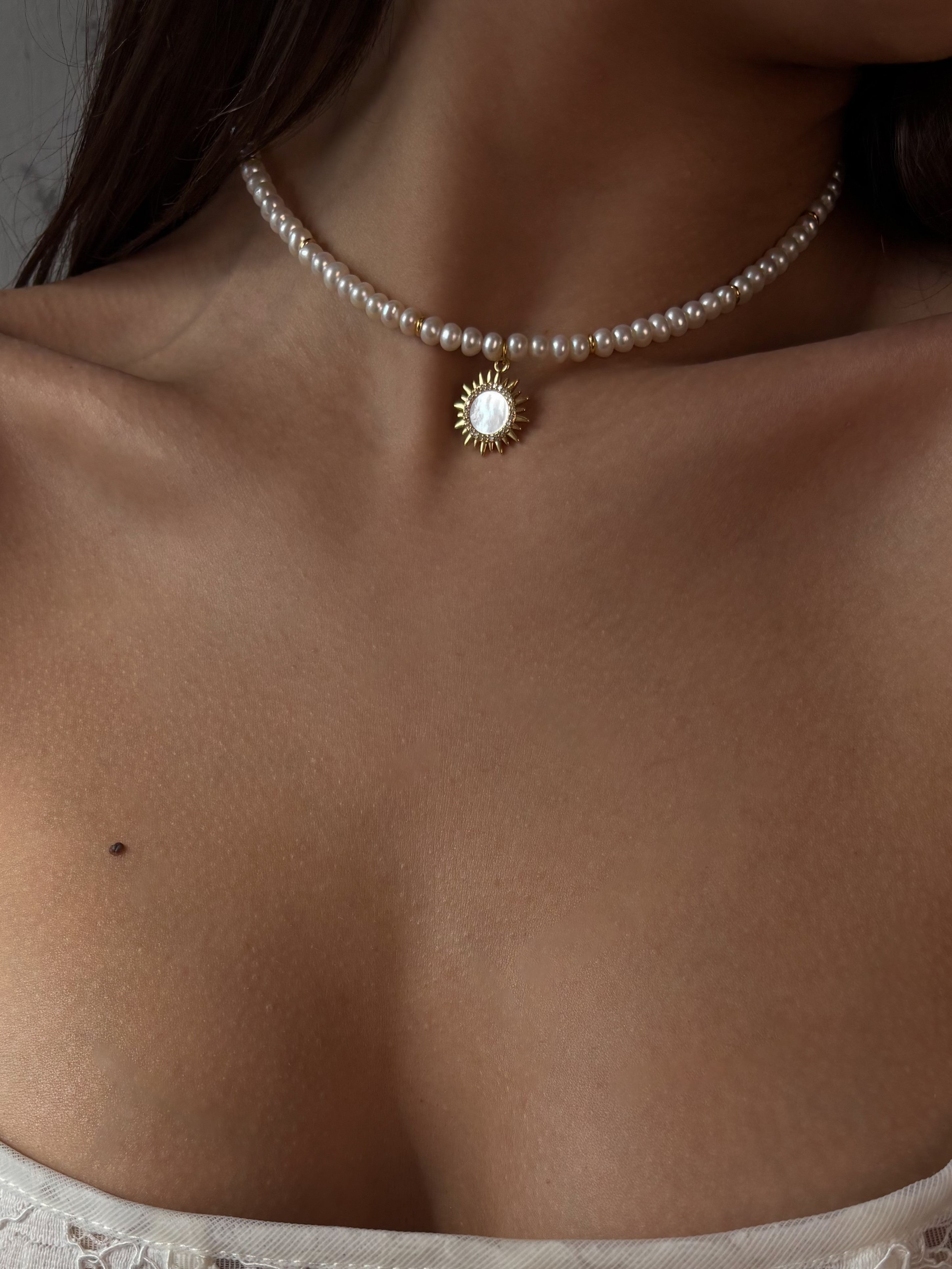 Pearl necklace with a sun pendant on a person's neck