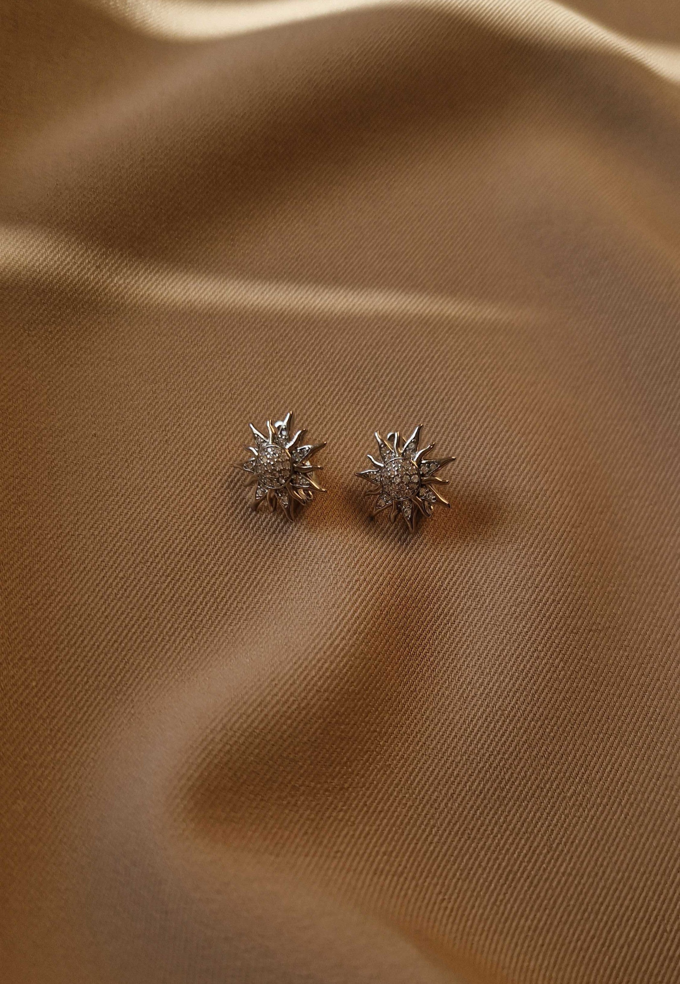Pair of sun-shaped earrings on a beige fabric background