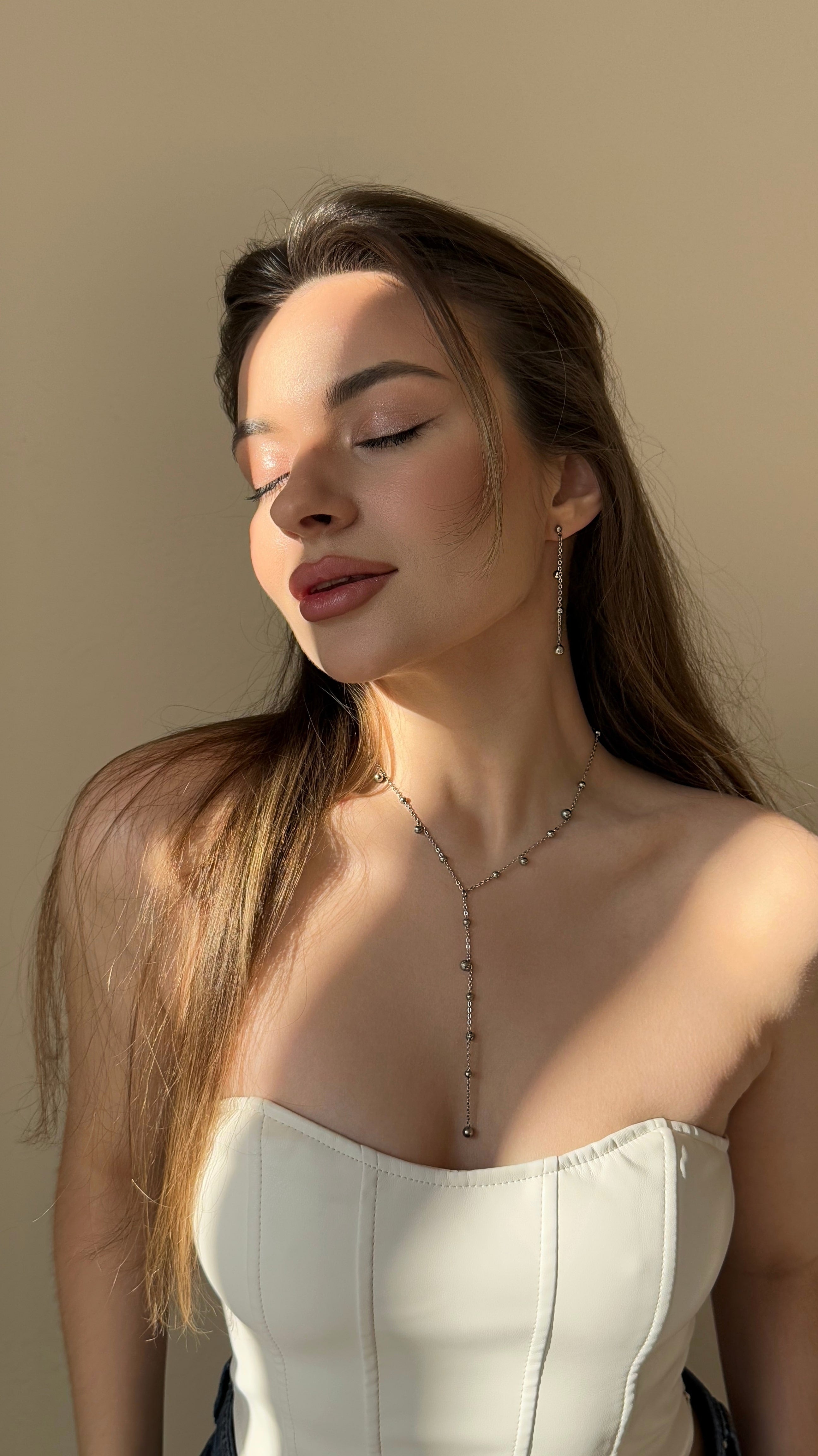 Woman wearing a delicate necklace against a neutral background