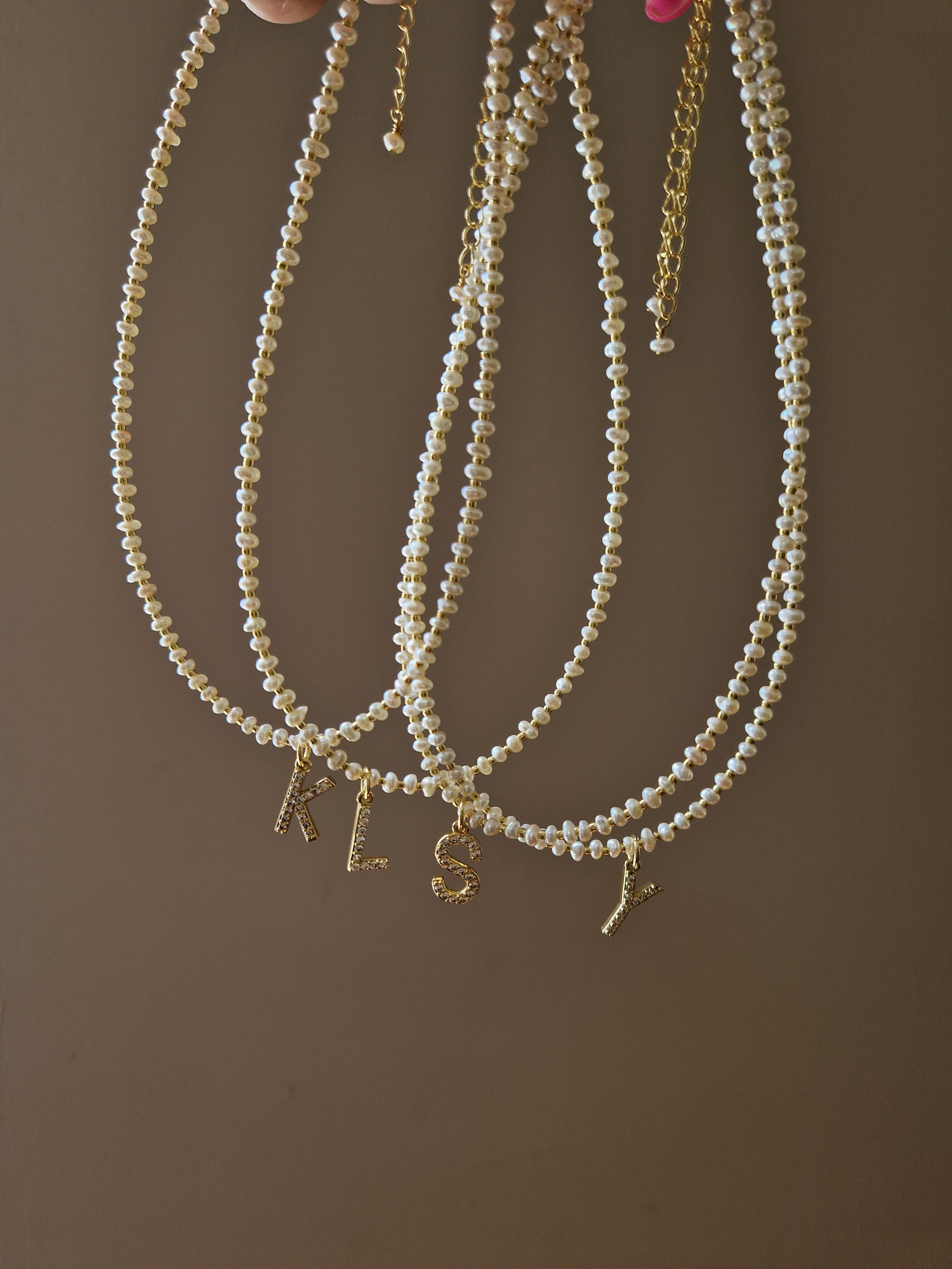 Pearl necklaces with letter pendants arranged on beige fabric
