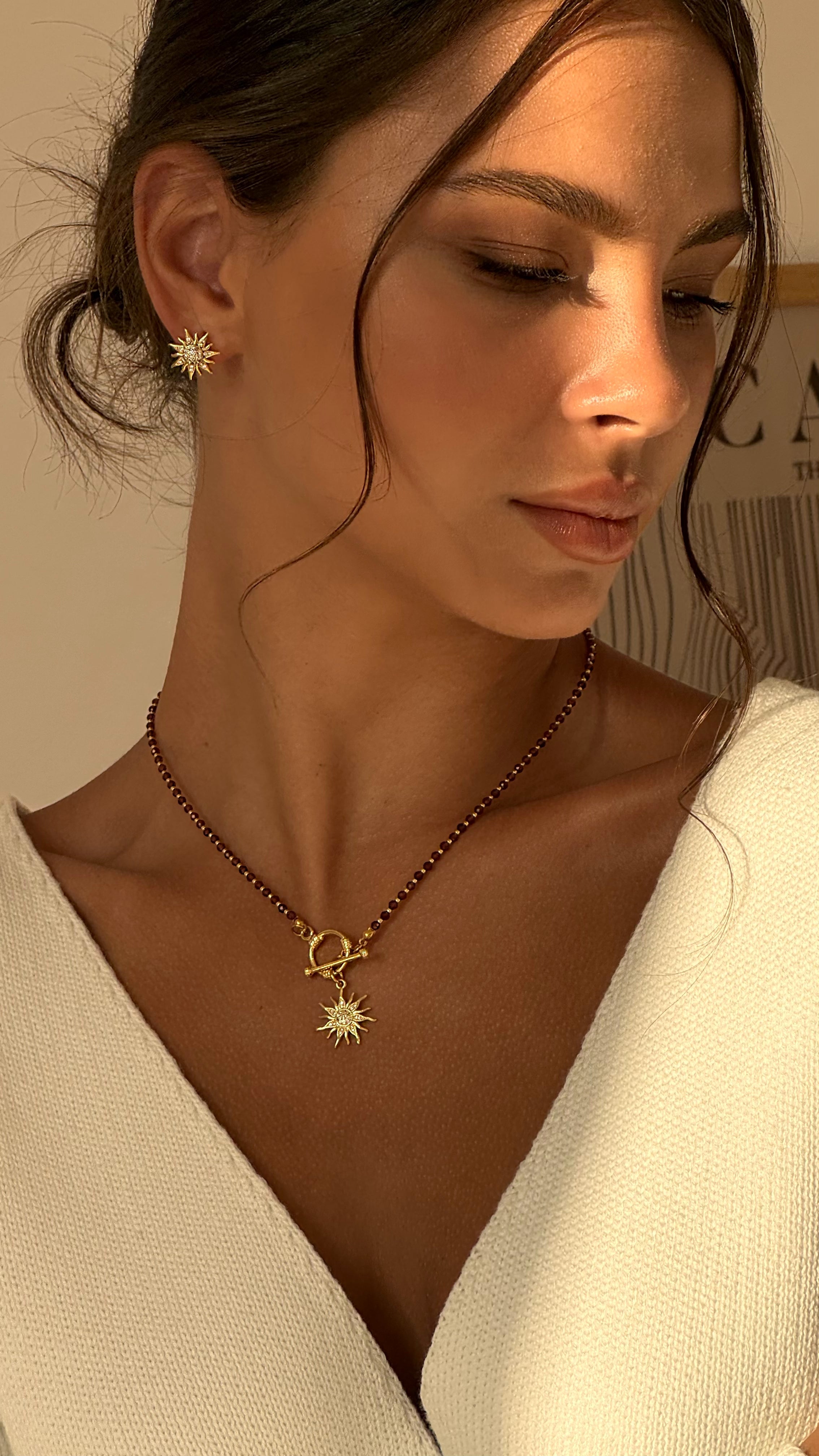 Woman wearing a necklace with a sun pendant and a matching earring.