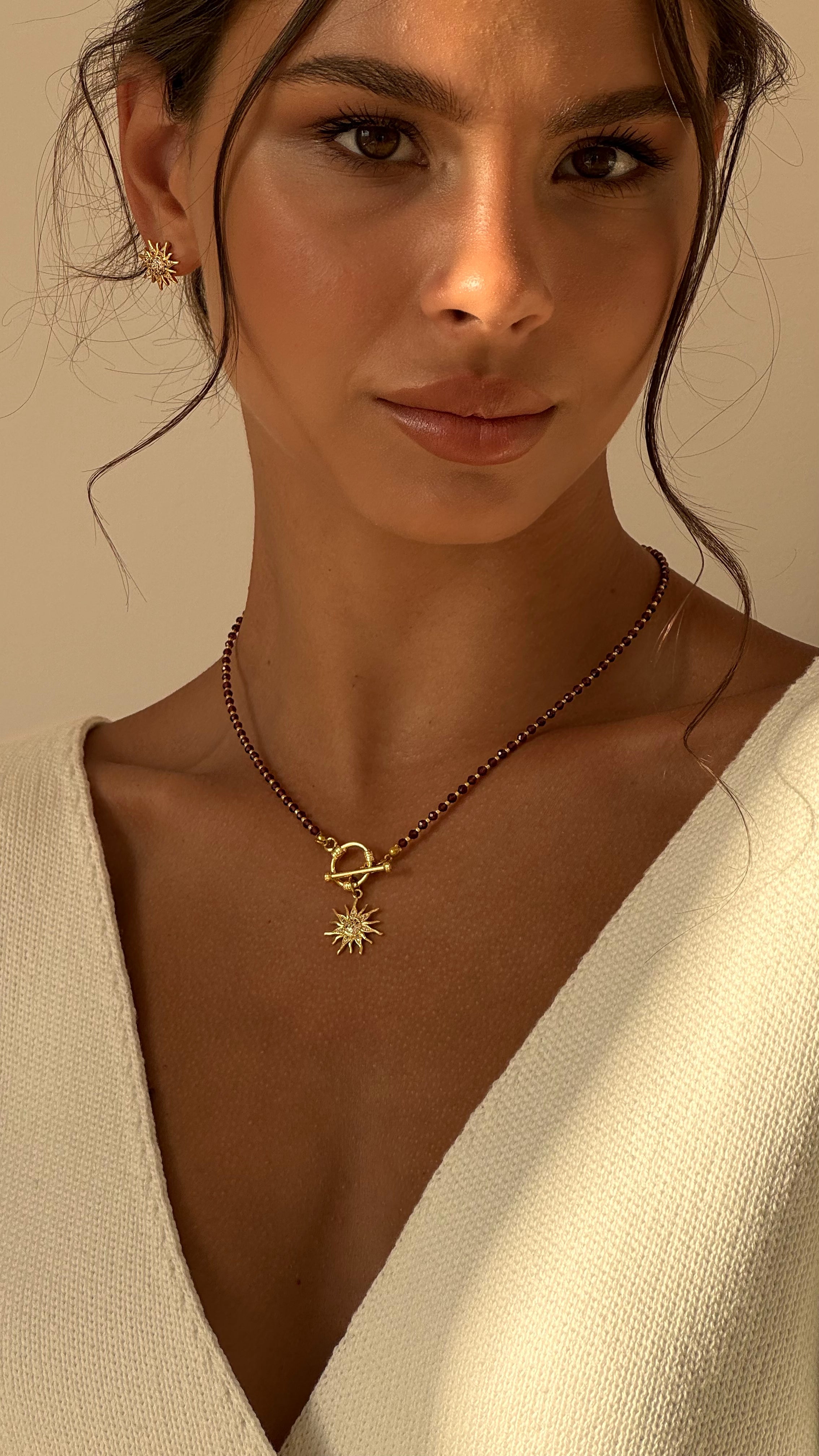 Woman wearing a red beaded necklace with a sun pendant against a neutral background