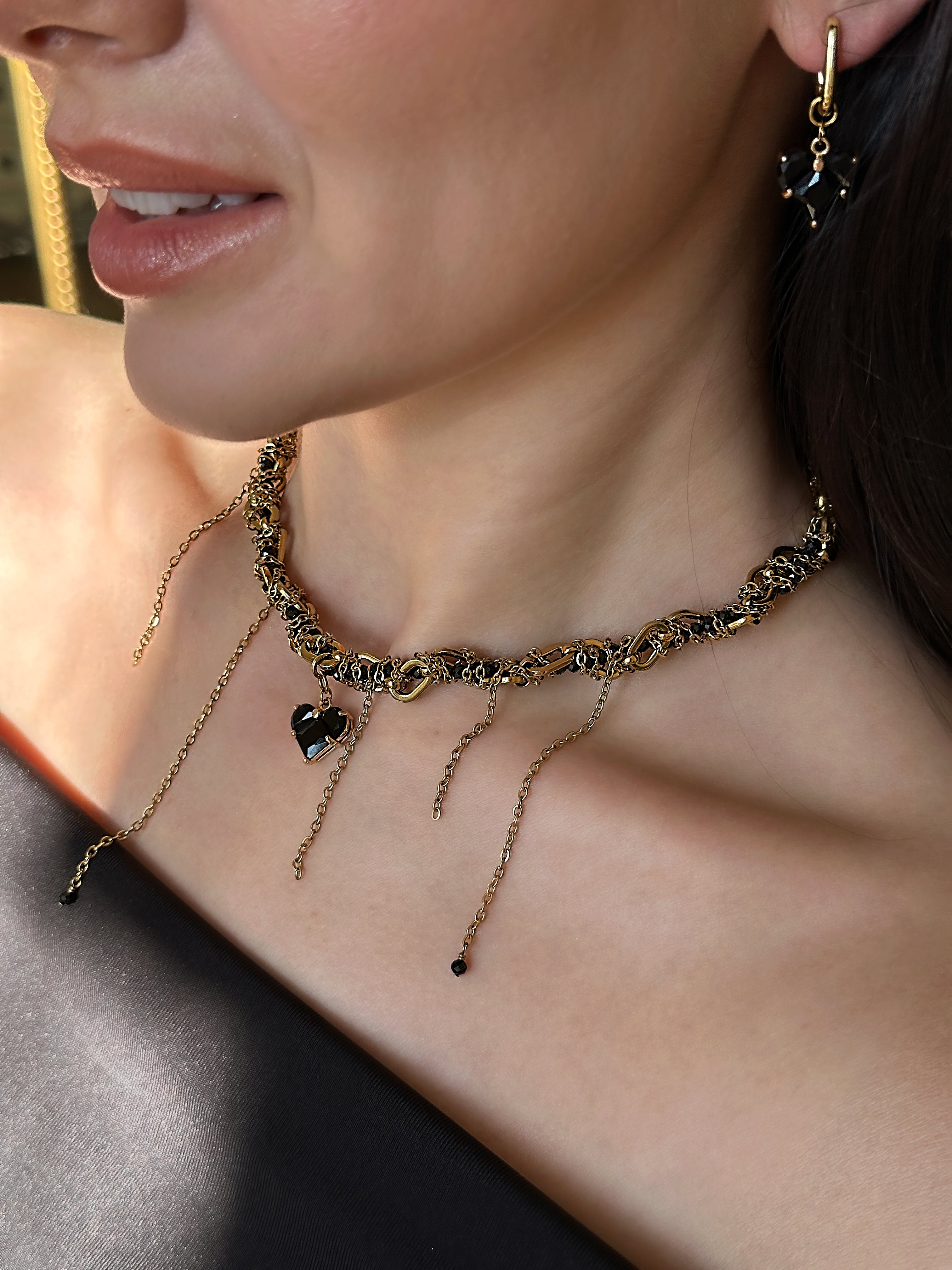 Close-up of a woman wearing a delicate gold-plated and black necklace with a heart pendant.