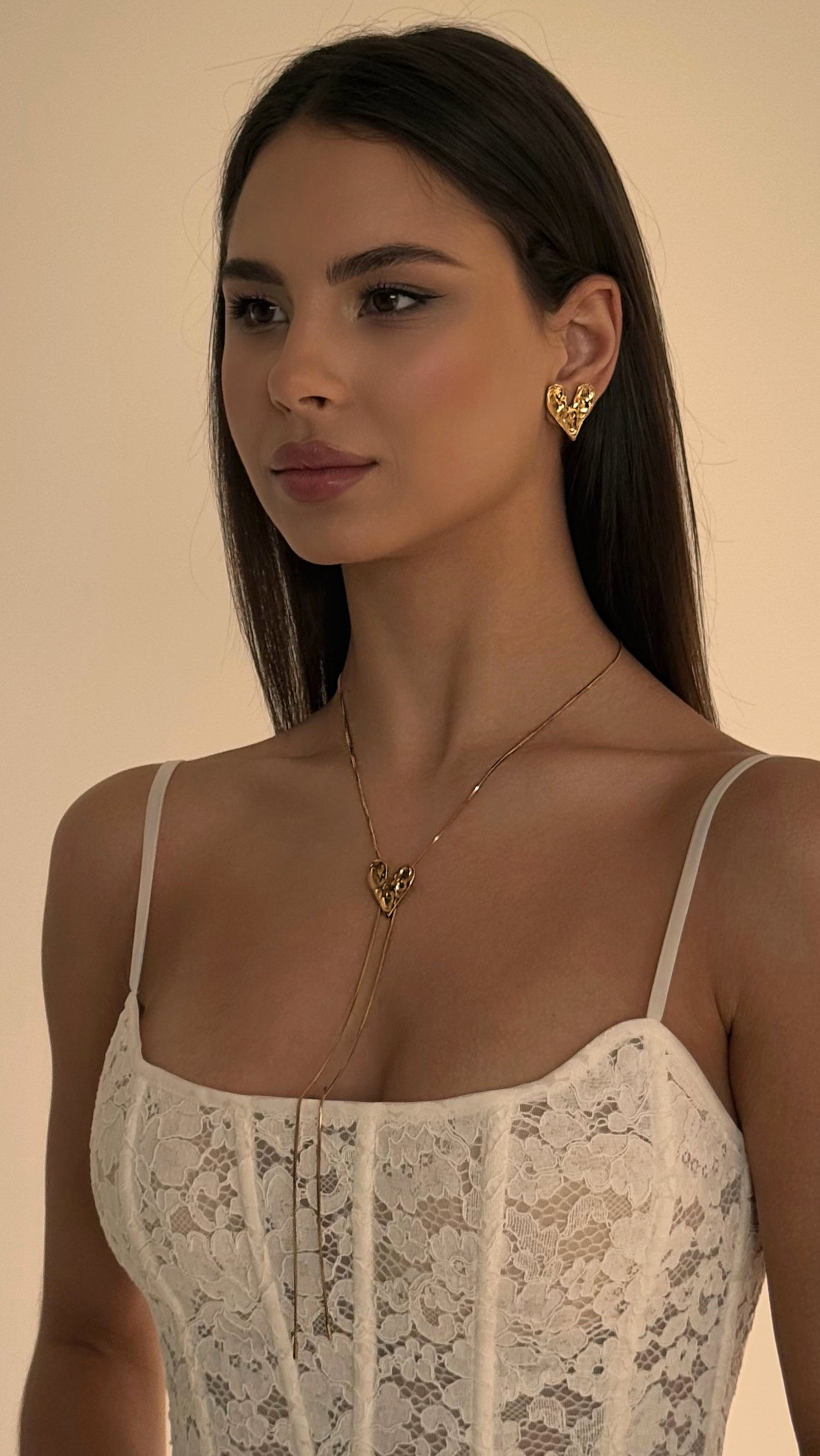 Woman wearing a lace top and gold jewelry against a beige background