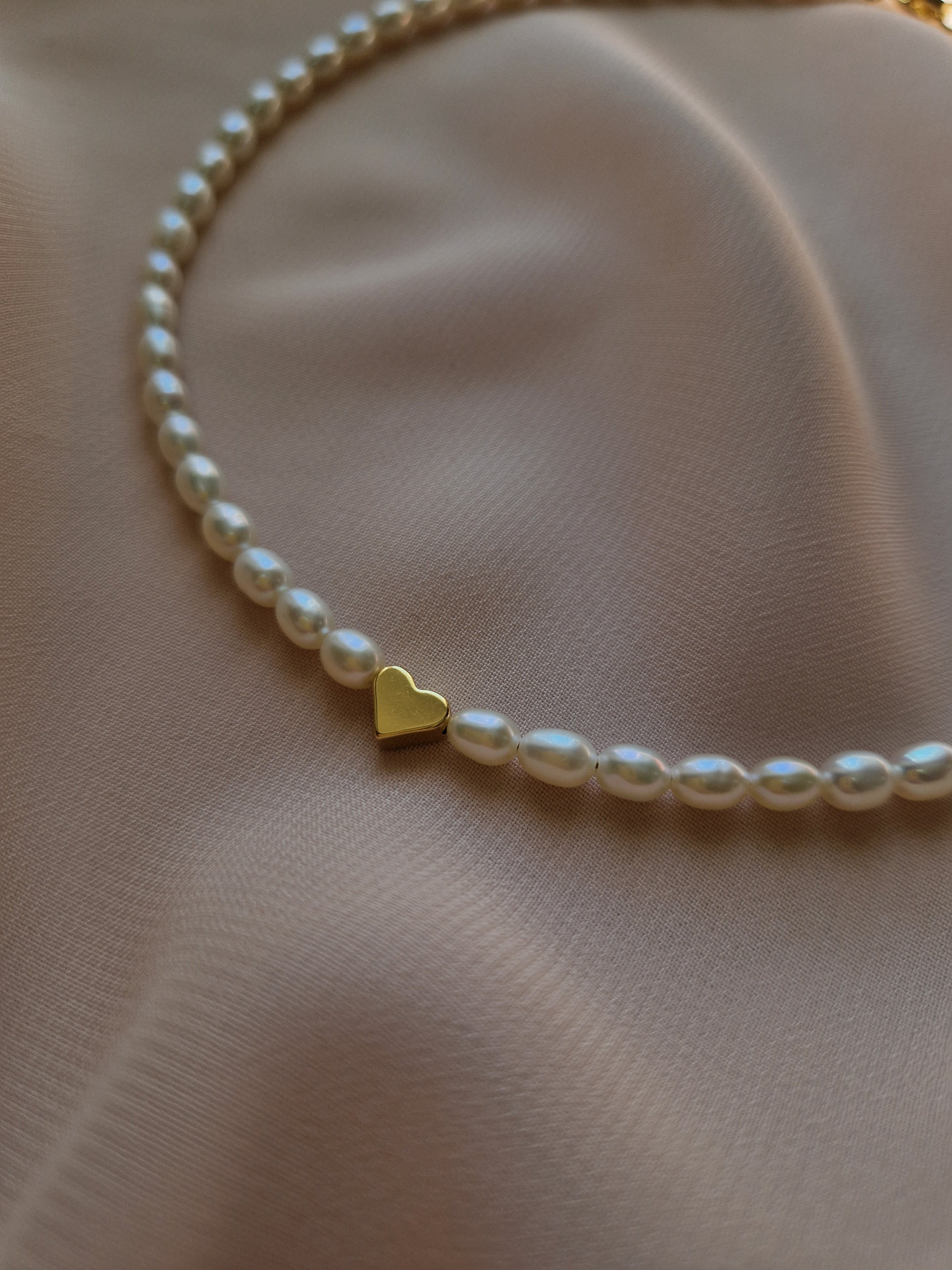 Pearl necklace with a gold-plated heart charm on a soft pink fabric background