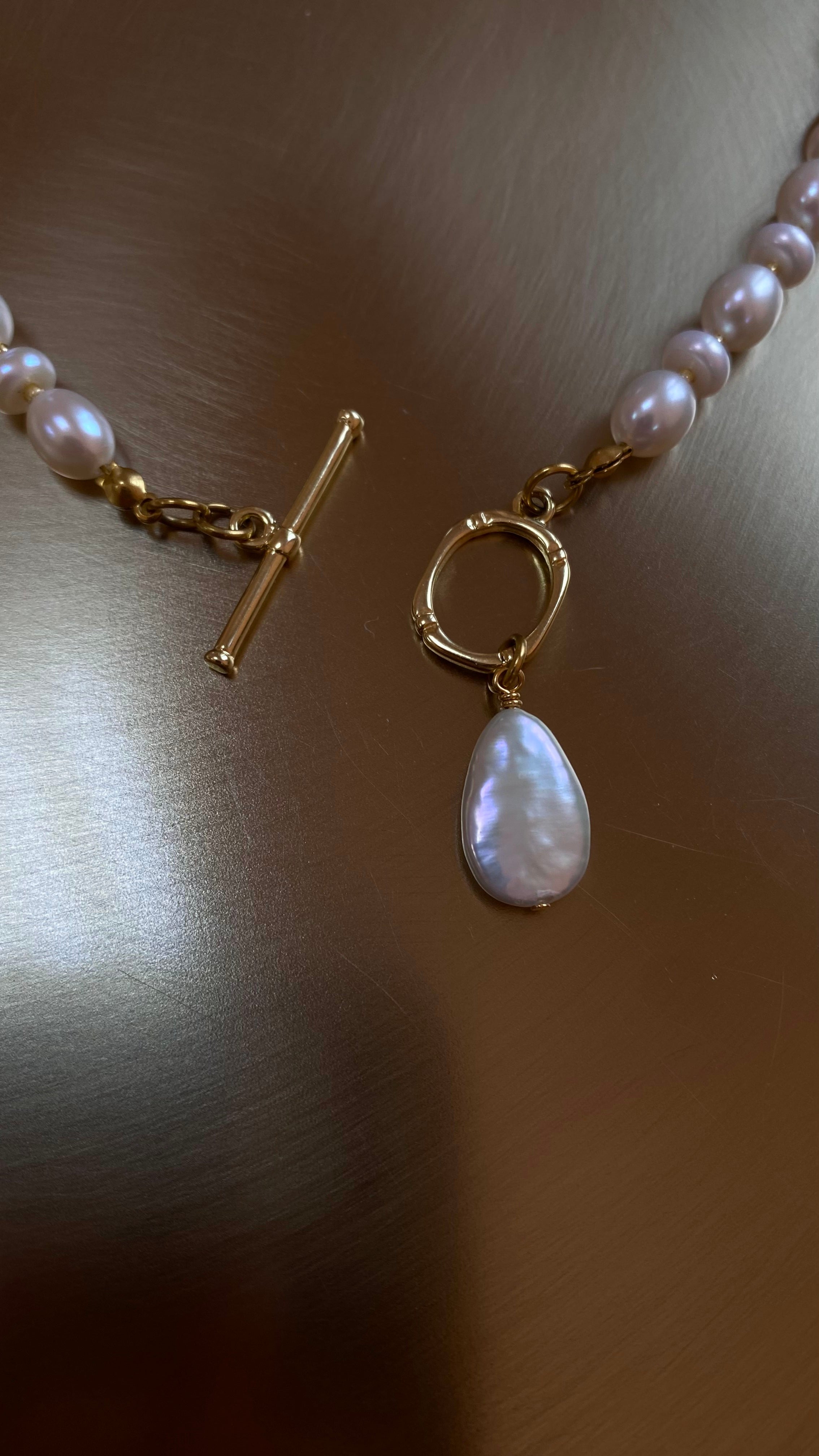 Pearl necklace with a gold-plated clasp and pendant on a neutral backgroun