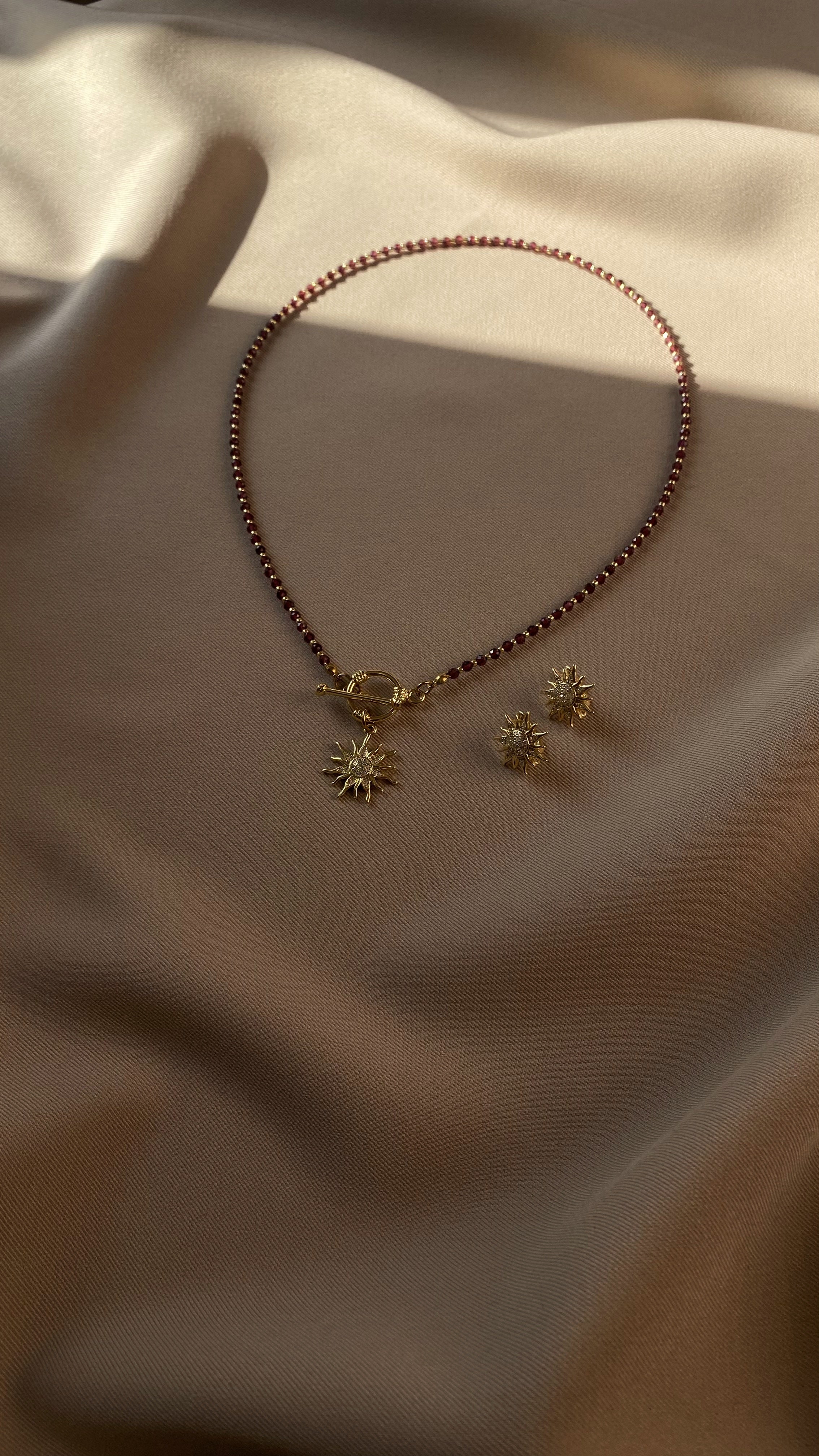 Garnet with gold-plated necklace and earrings on a beige fabric background