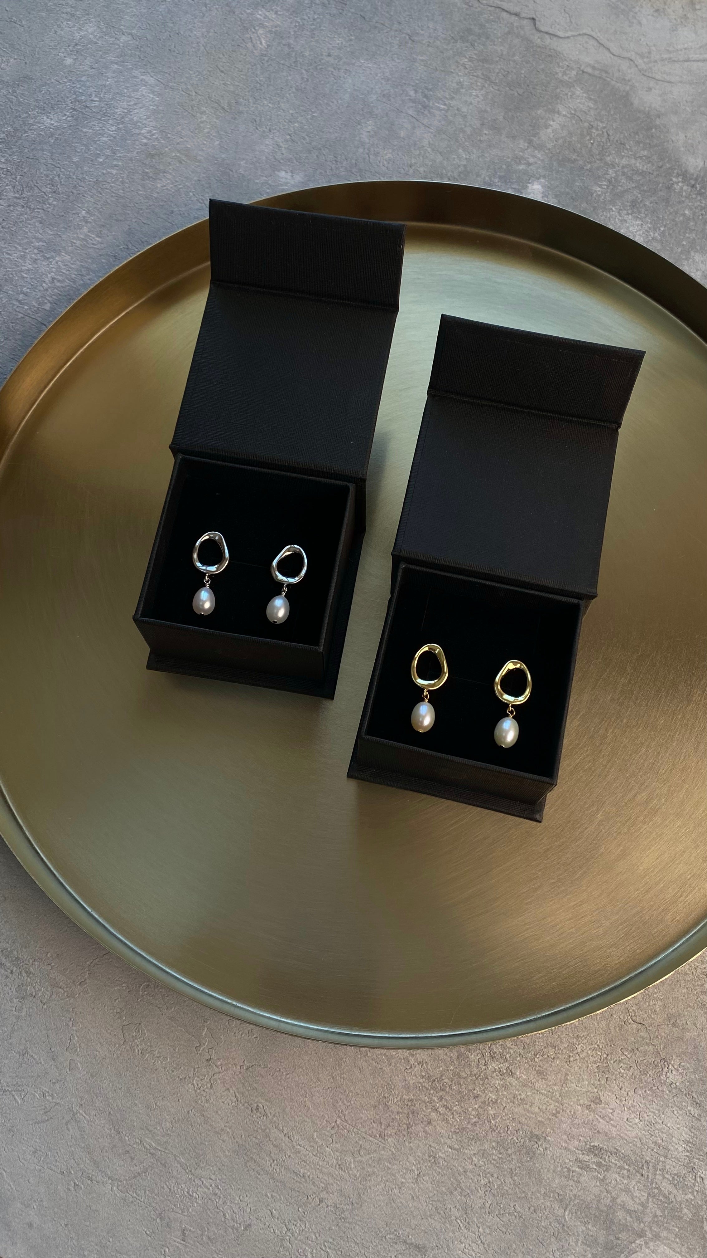 Pair of earrings in black boxes on a reflective surface