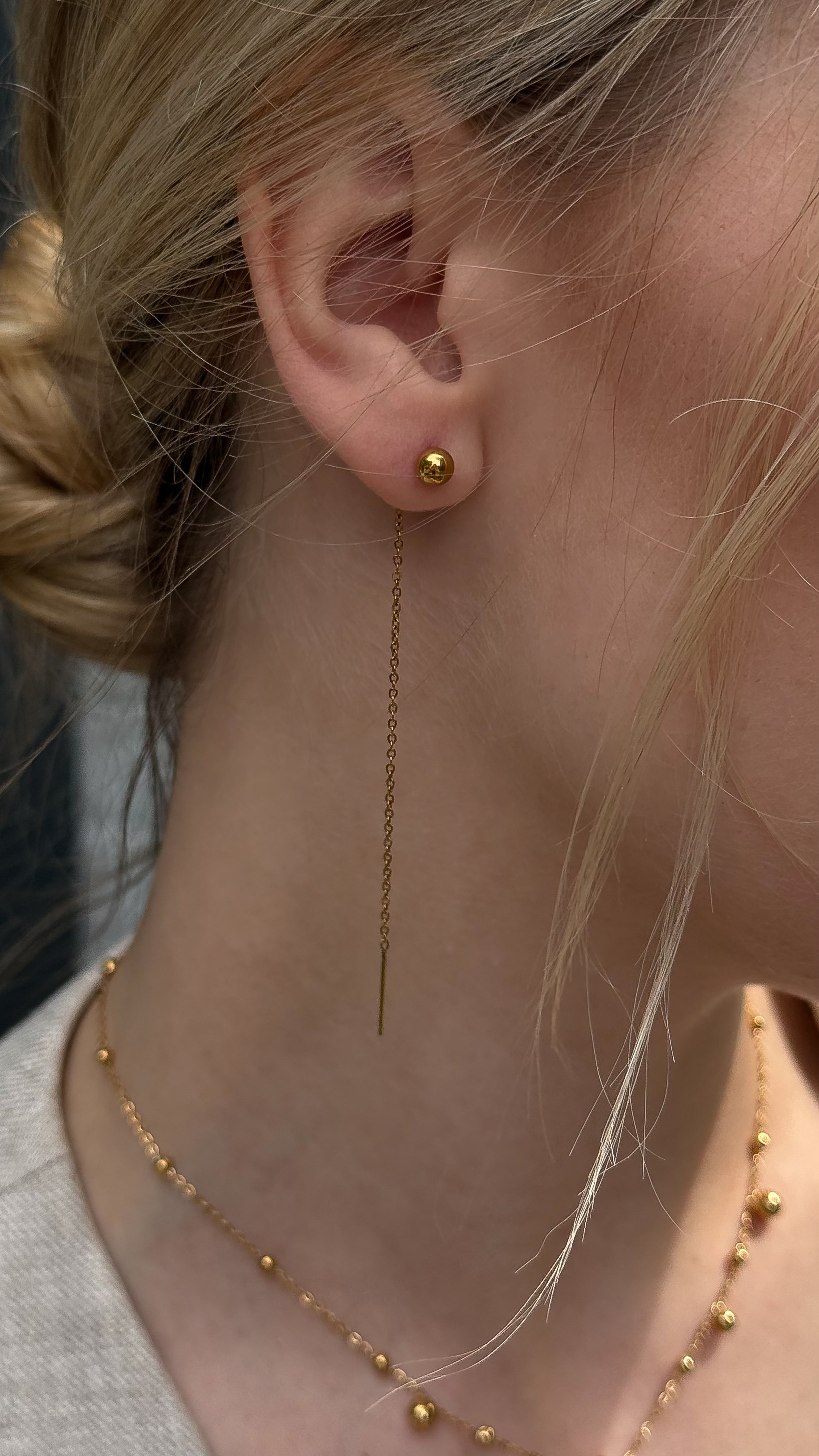 Close-up of a person wearing gold-plated earrings and a necklace with a blurred background