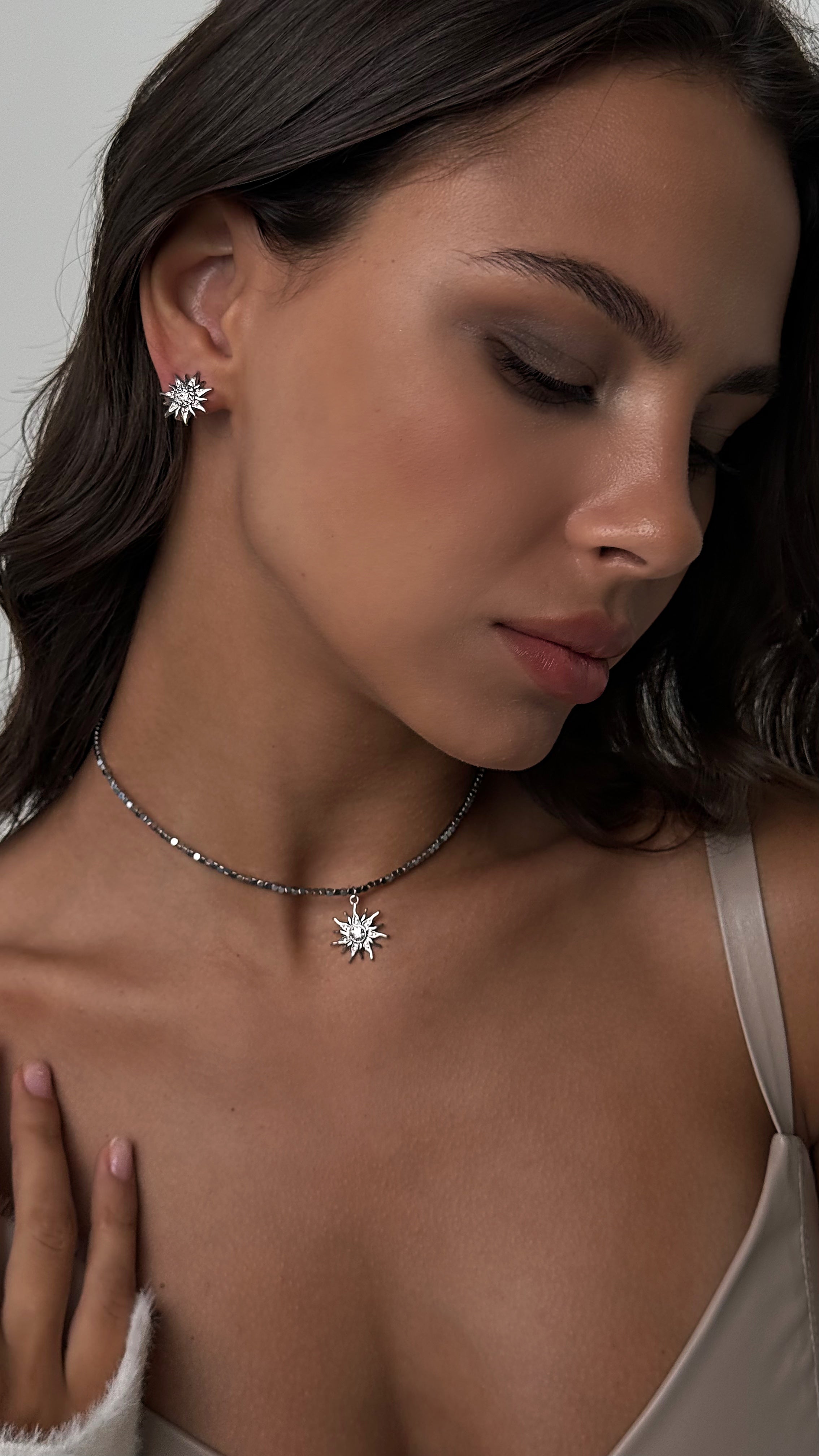Woman wearing sun-shaped earrings and a necklace with a neutral background