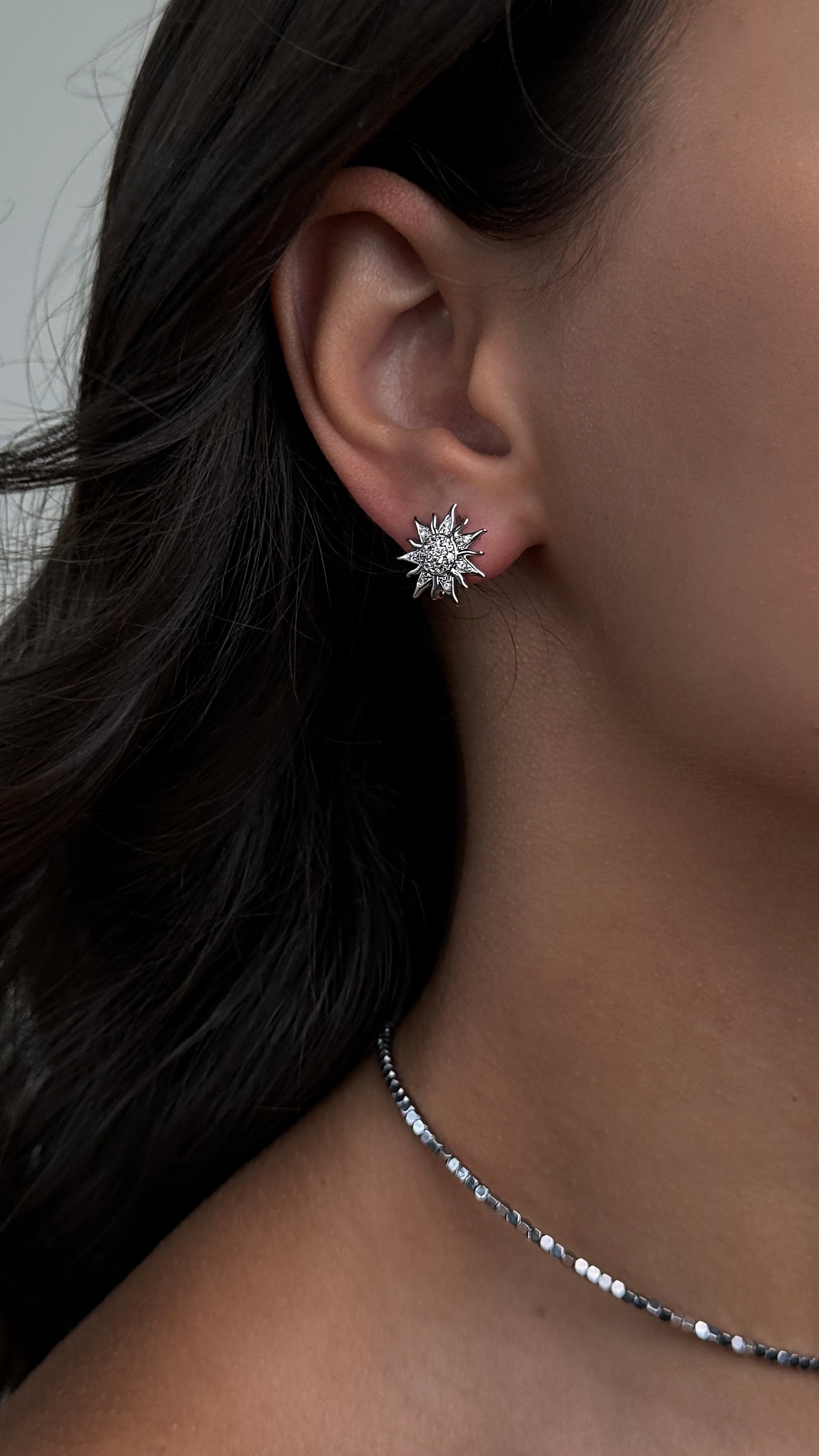 Close-up of an ear wearing a sun-shaped earring with a blurred background