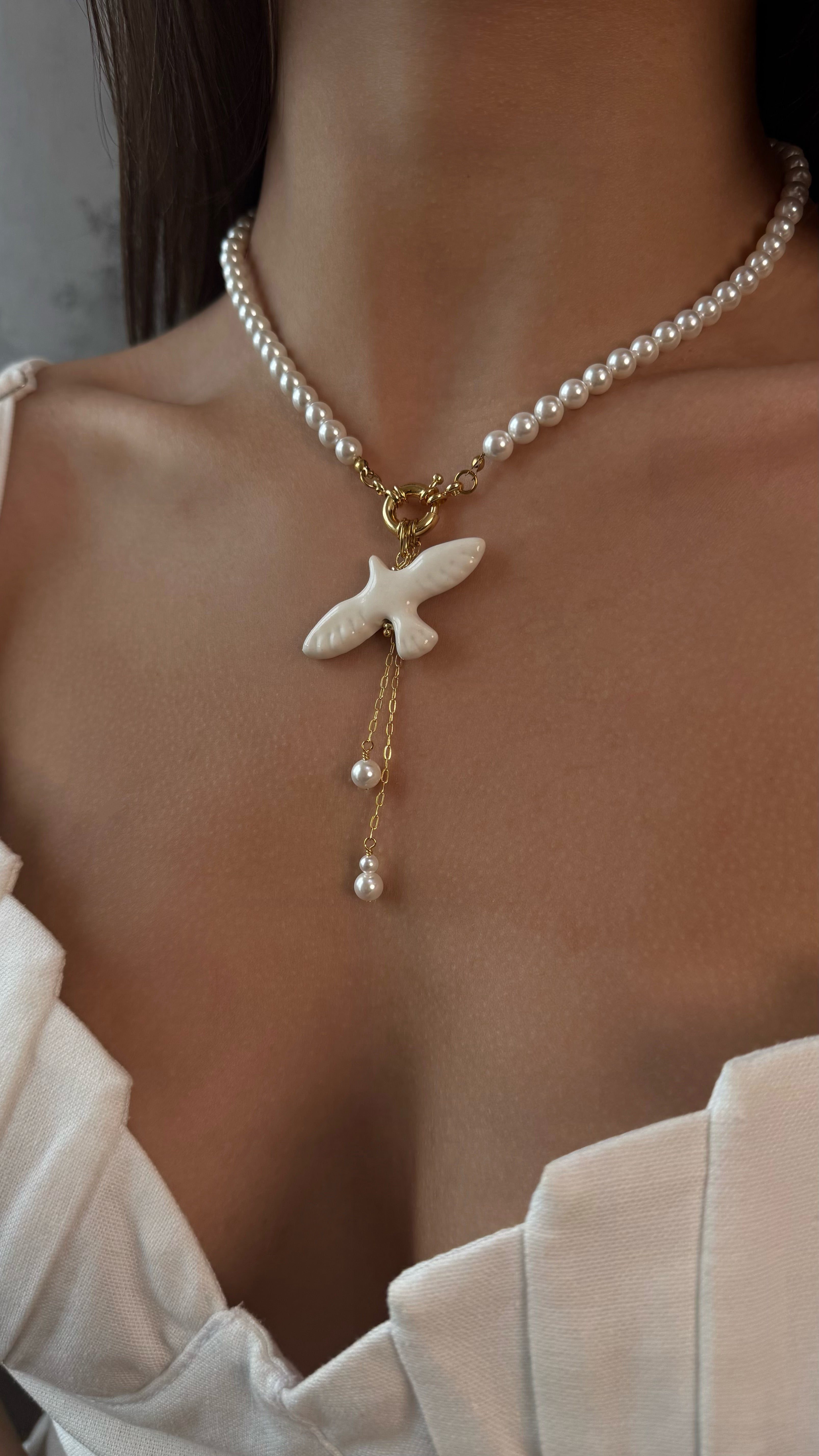 Pearl necklace with a white bird pendant worn by a person in a white outfit.