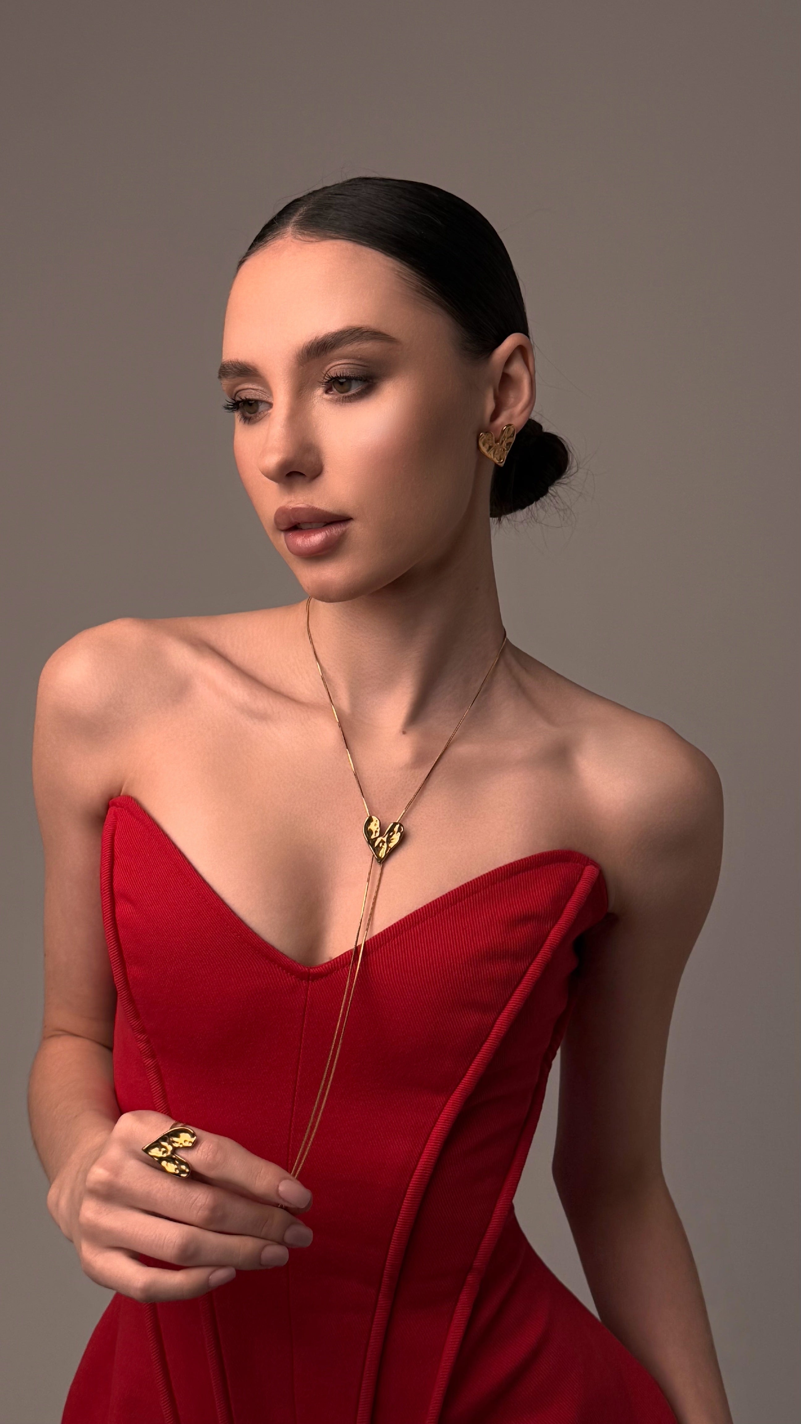 Woman wearing a red dress with a necklace and earrings against a neutral background