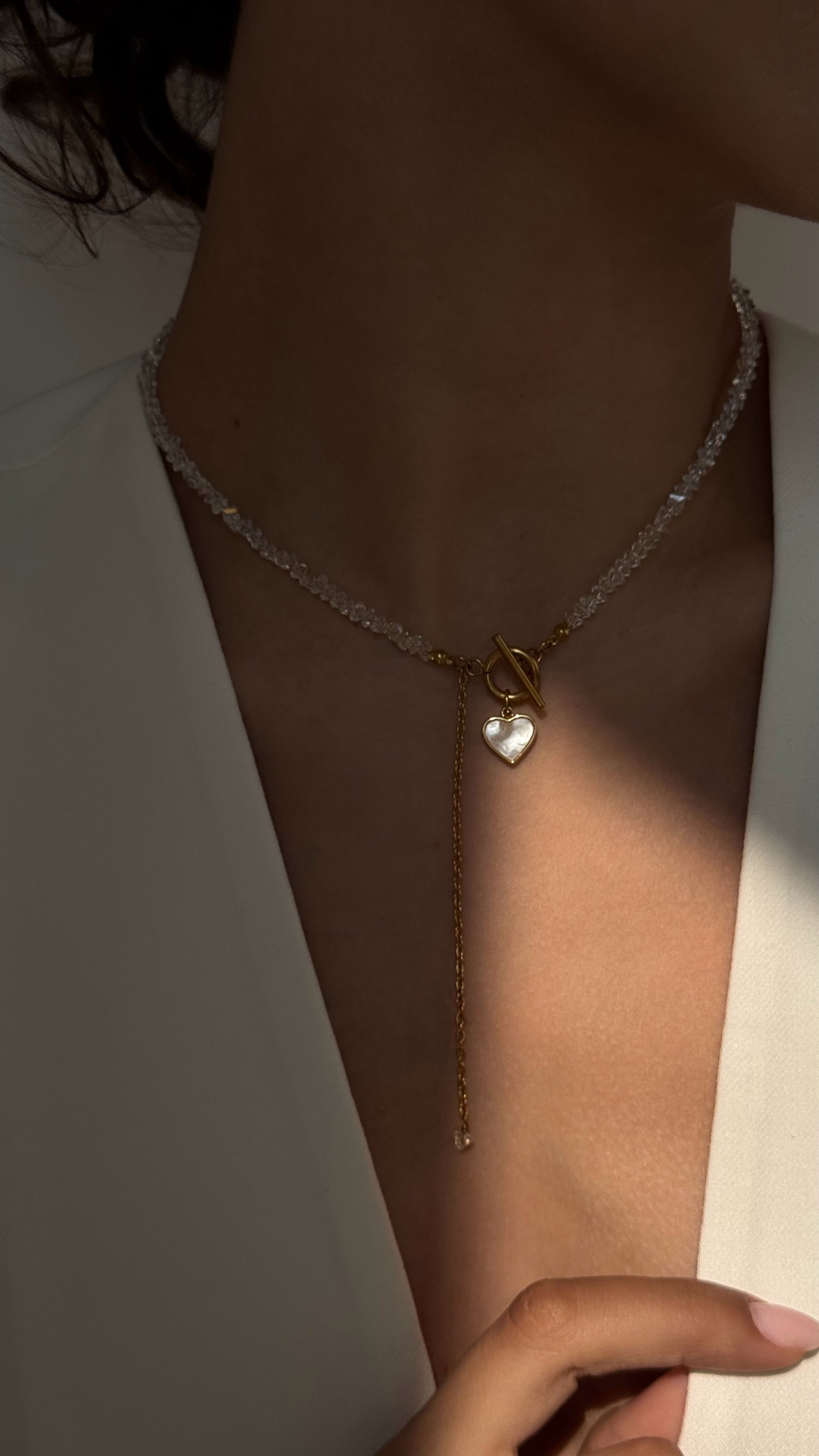 Necklace with a heart-shaped pendant on a person wearing a white outfit.