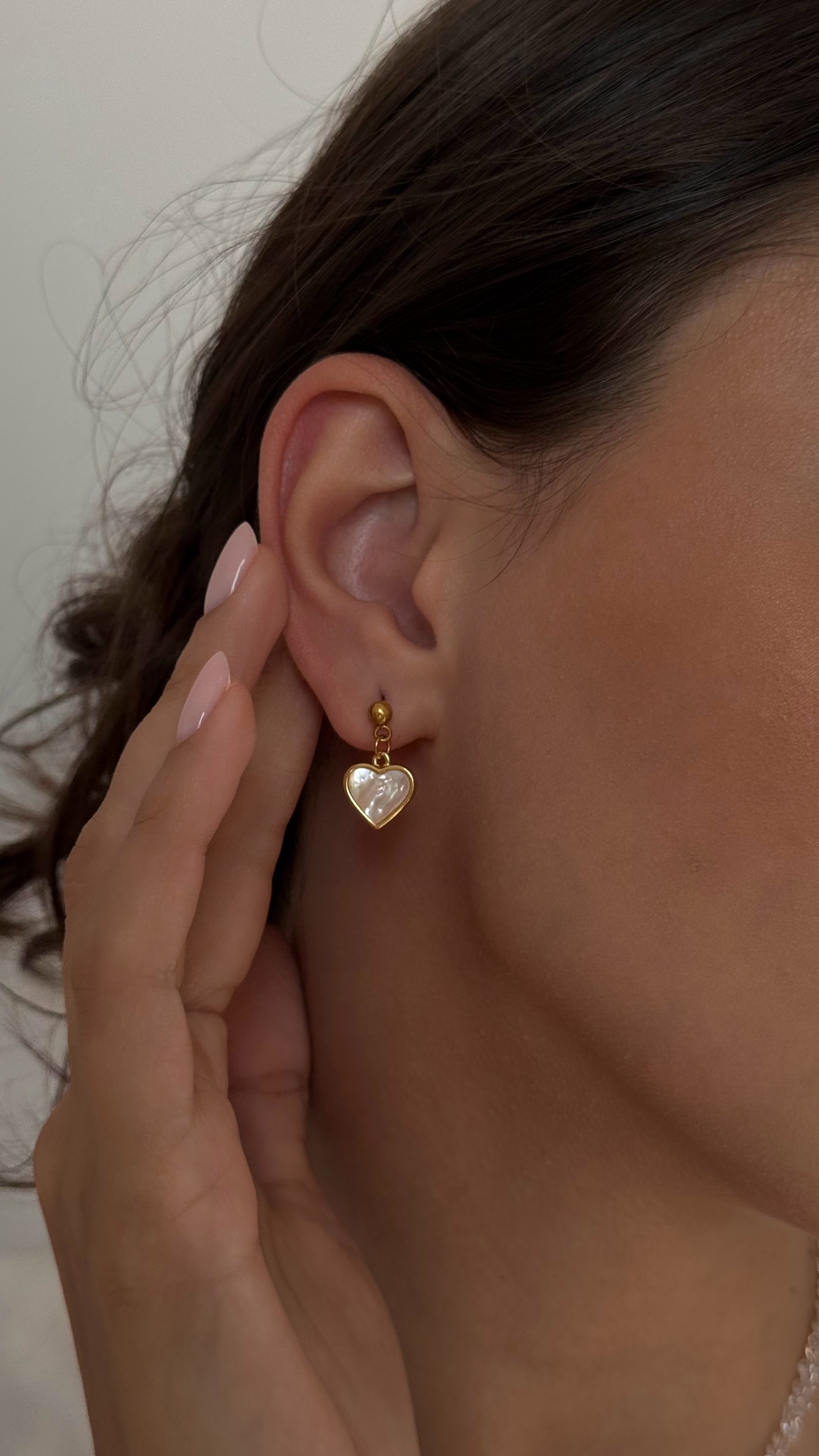 Heart-shaped earring worn by a person with a neutral background