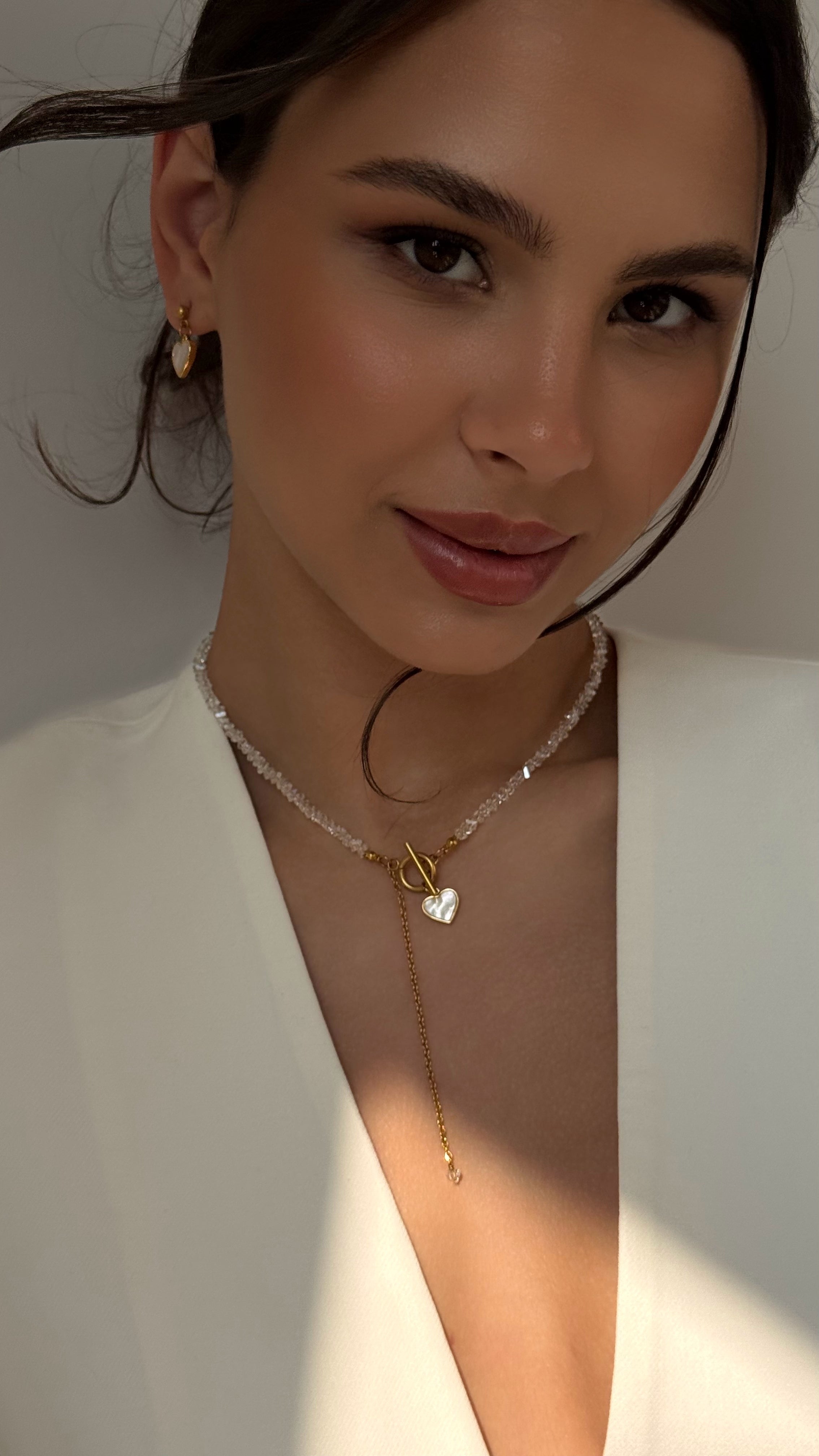 Woman wearing a delicate necklace with a heart pendant against a neutral background