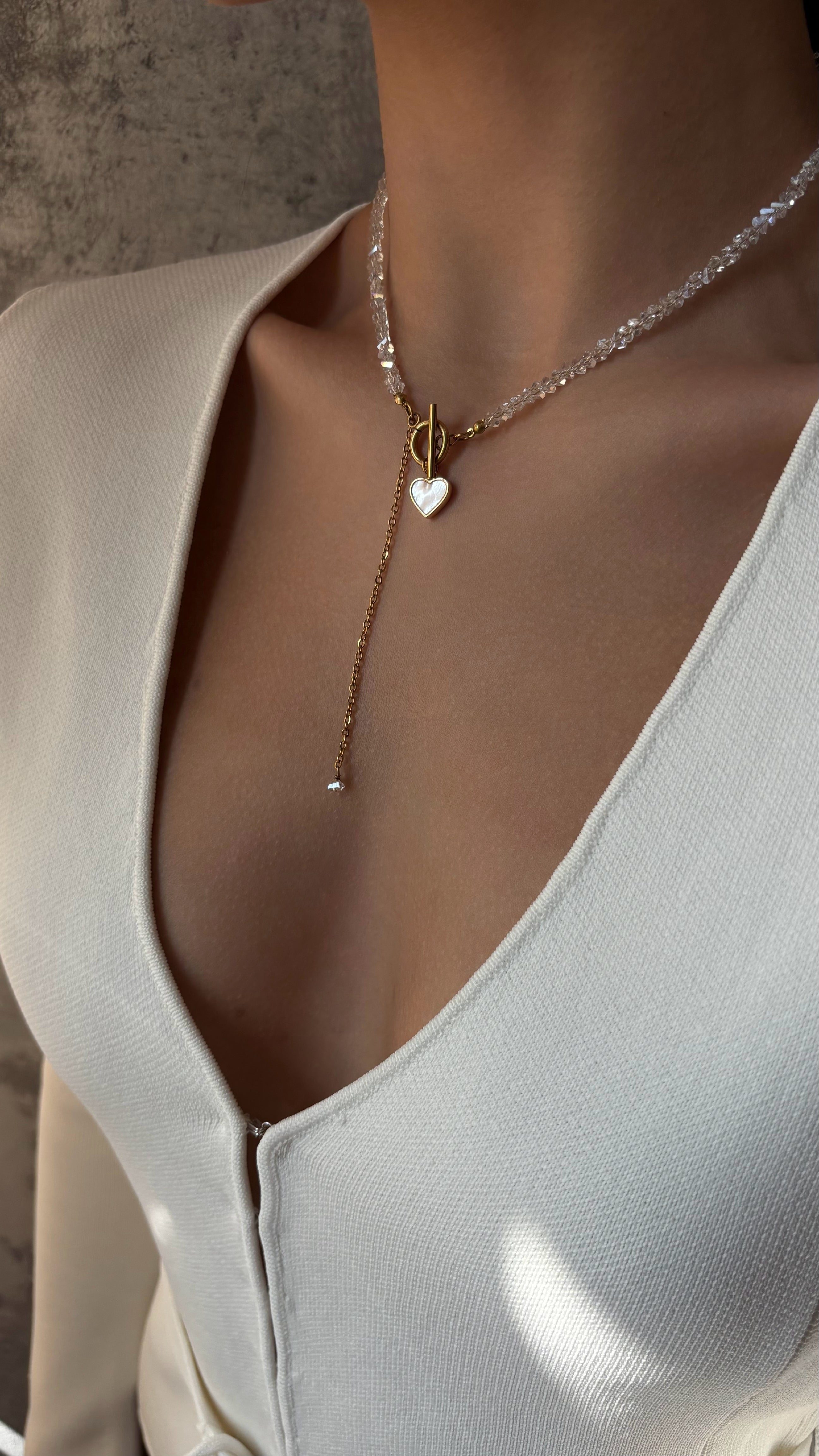 Necklace with a heart pendant worn by a person in a light-colored outfit.