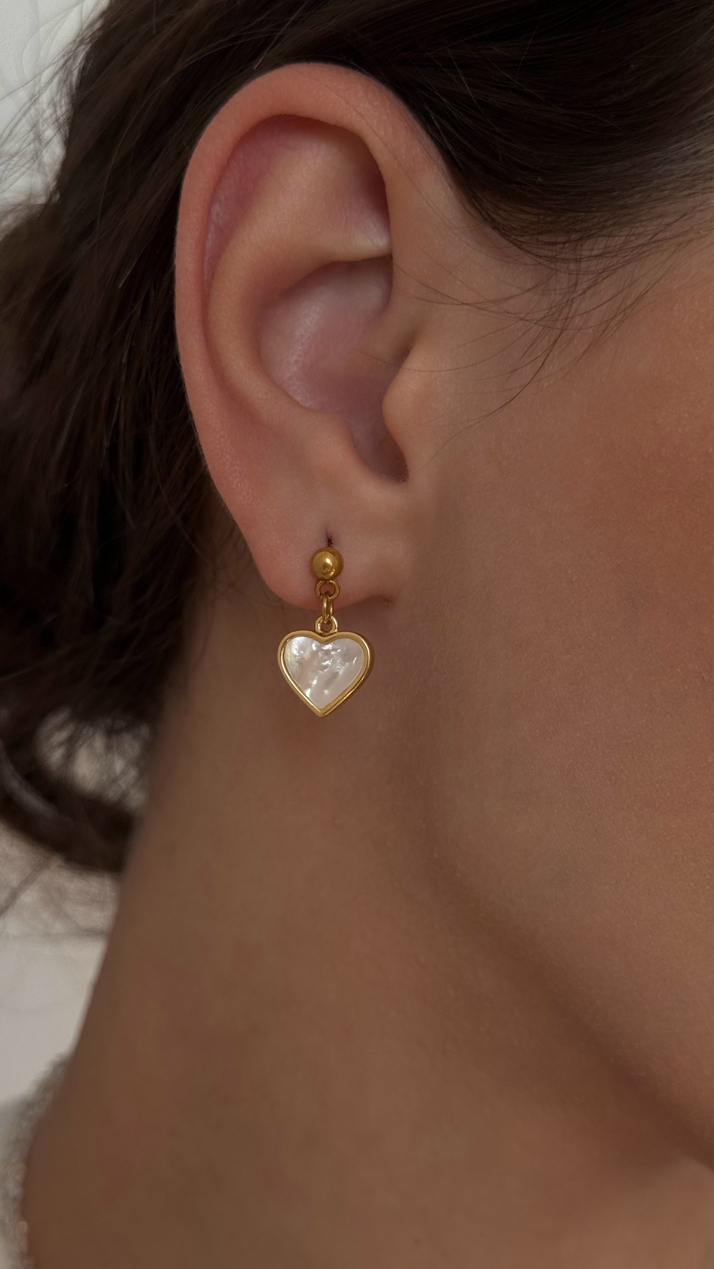 Delicate stud earrings with mother-of-pearl heart charms, offering a romantic and feminine touch with minimalist design and soft shimmer.