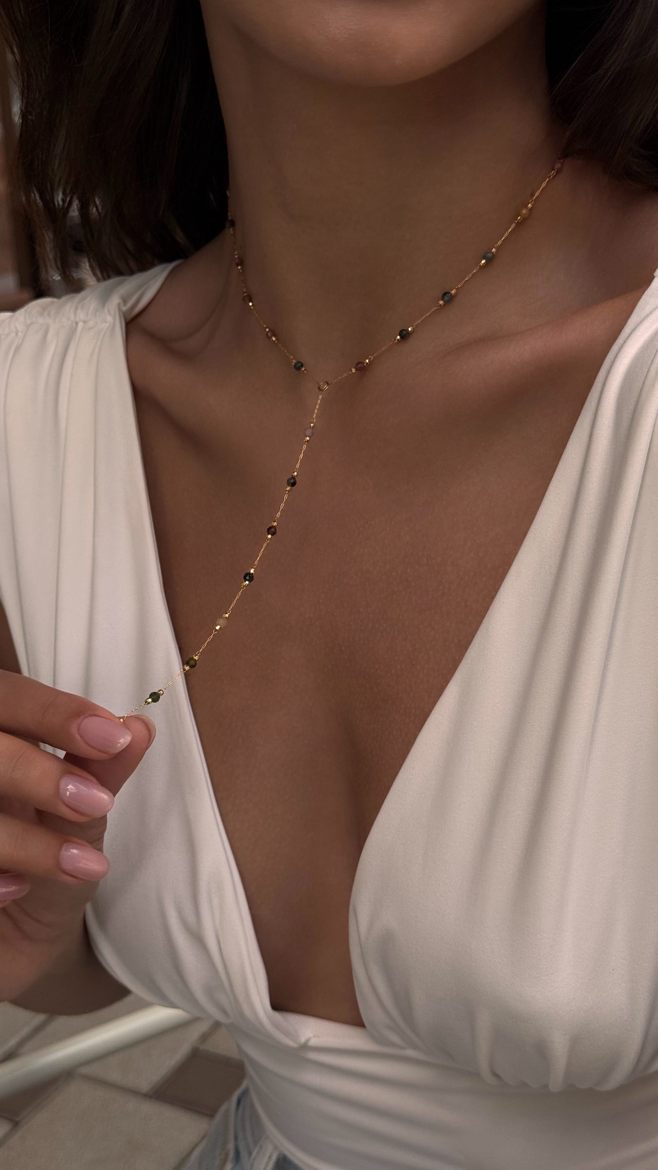 Close-up of a person wearing a delicate necklace with a white top.