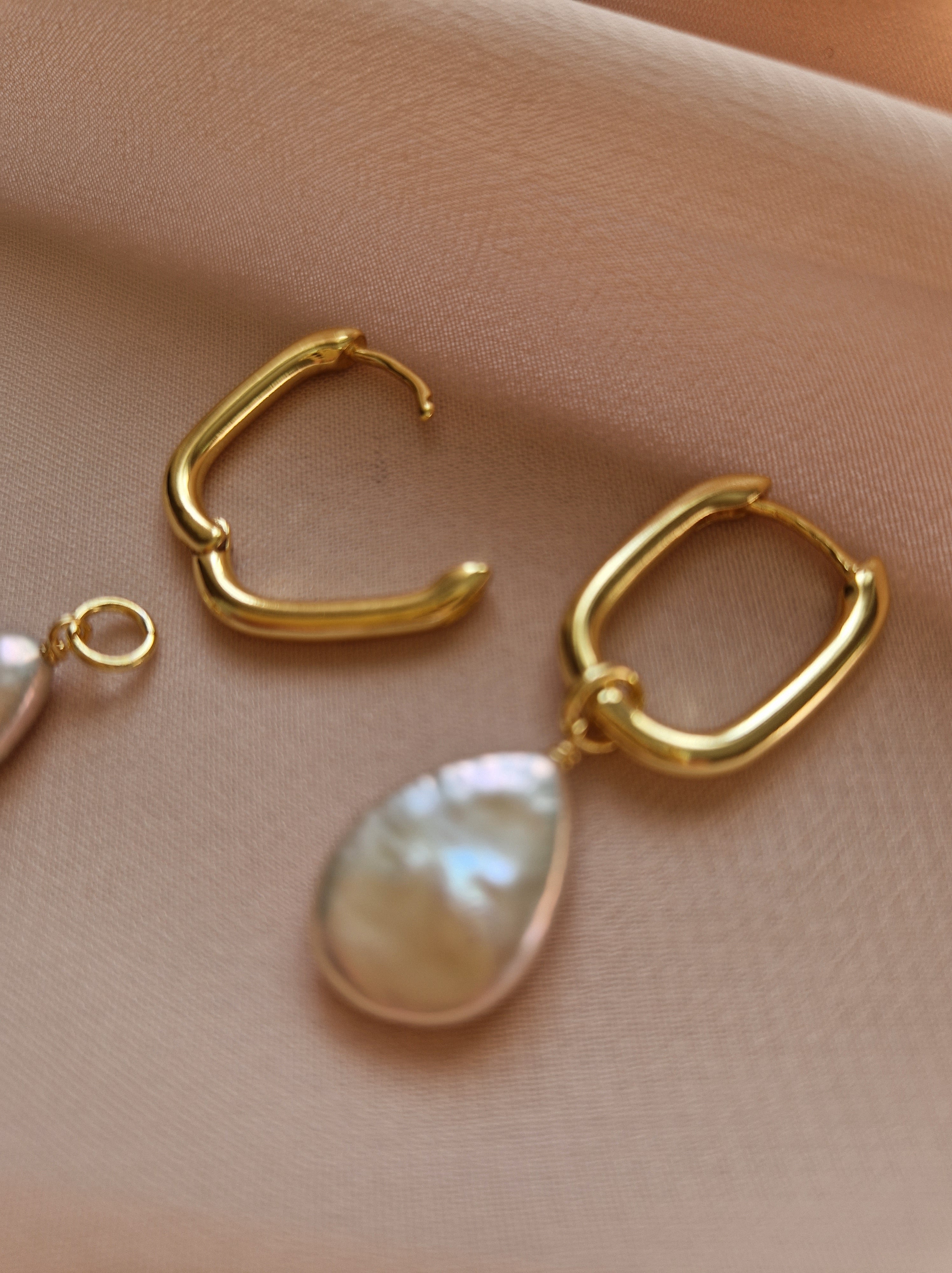 Gold-plated hoop earrings with pearl drops on a beige fabric background