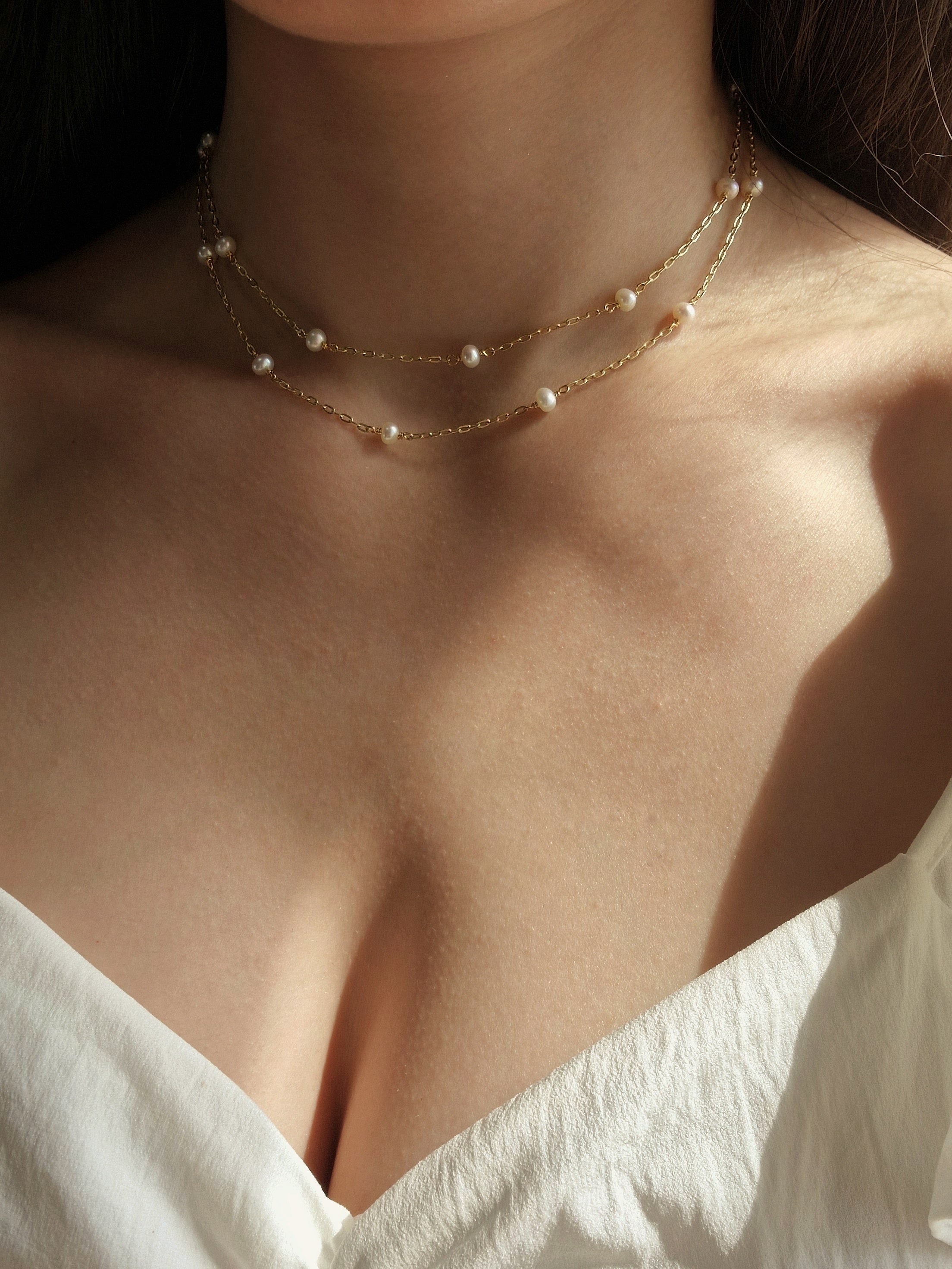 Delicate double-layered necklace featuring natural freshwater pearl accents, crafted from high-quality gold-plated brass for a warm and elegant feminine look.