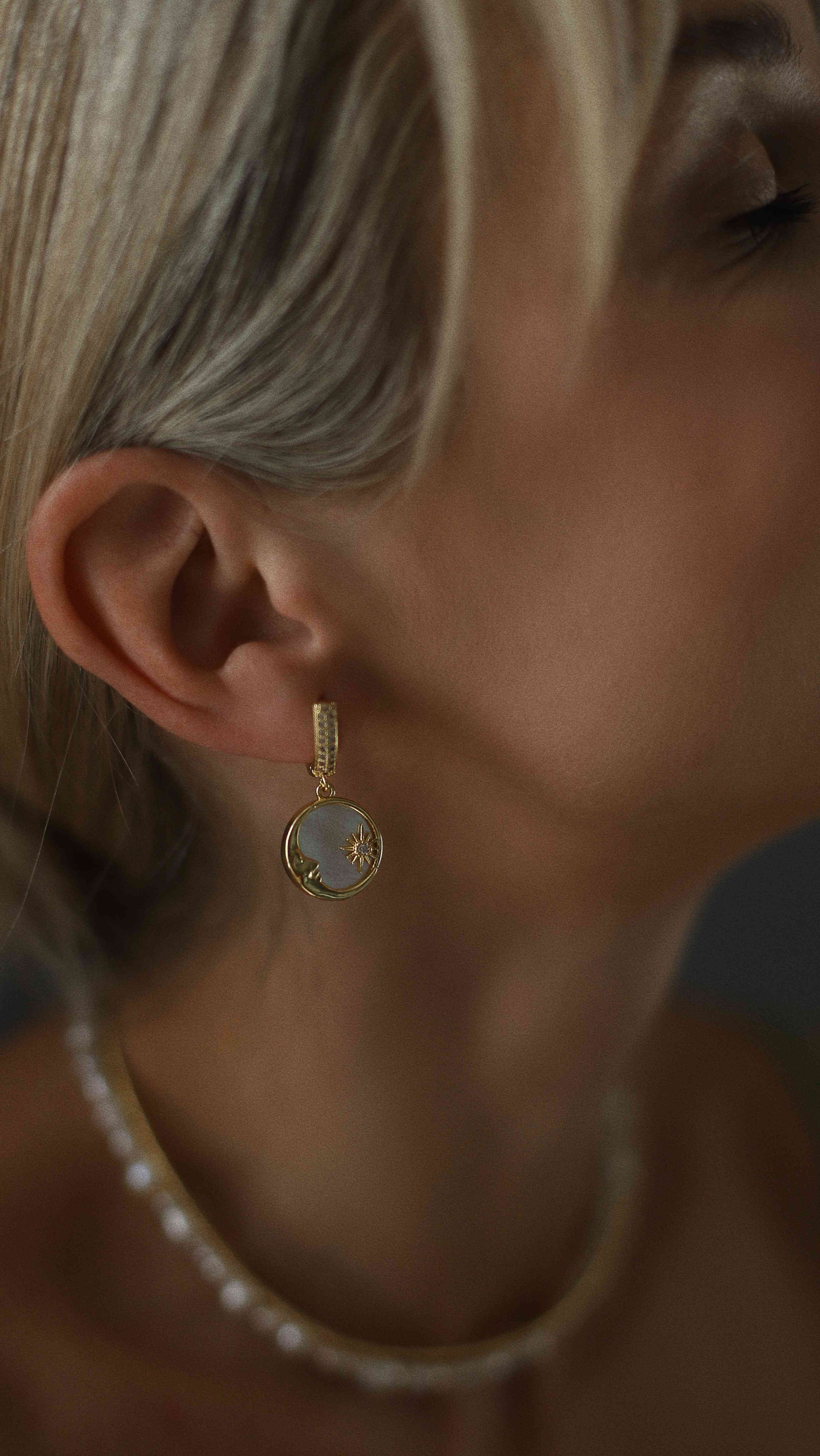Close-up of a person wearing a gold-plated earring with a gemstone.