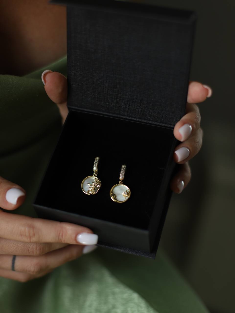 Person holding a black jewelry box with gold earrings inside