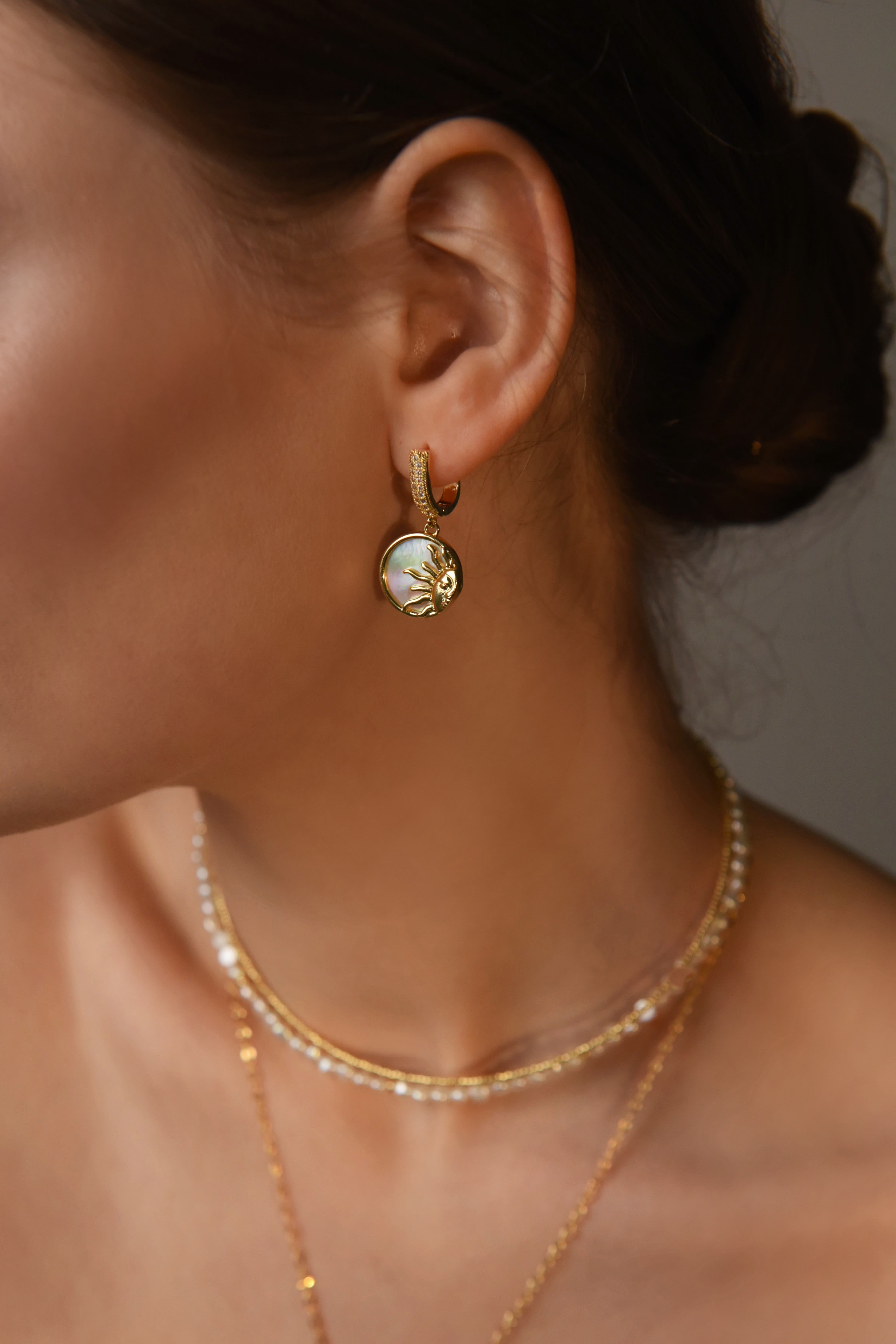 Close-up of a person wearing gold-plated hoop earrings and necklaces.