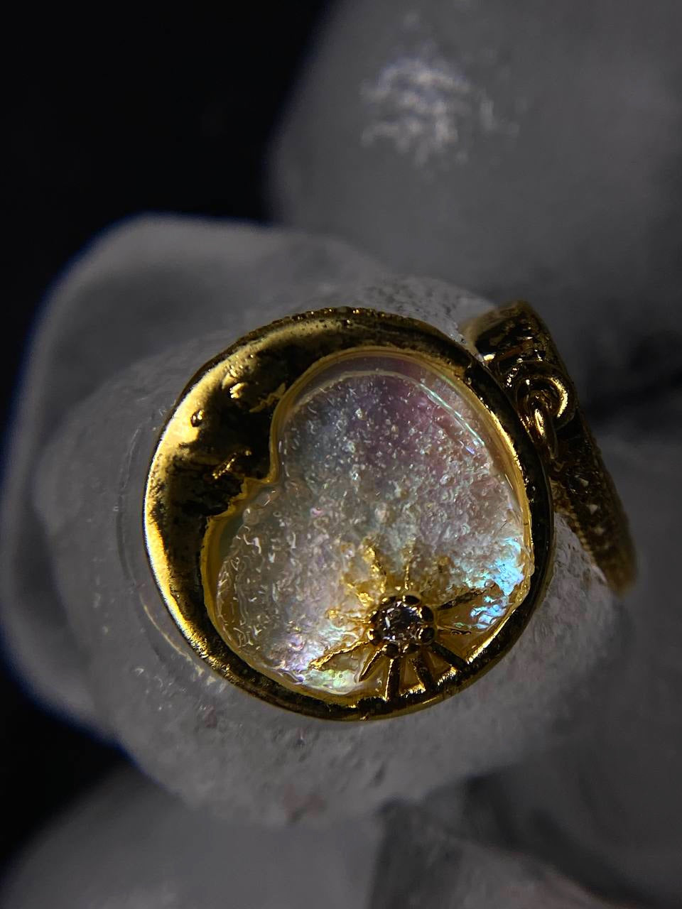 Gold ring with a heart-shaped gemstone and central diamond on a dark background