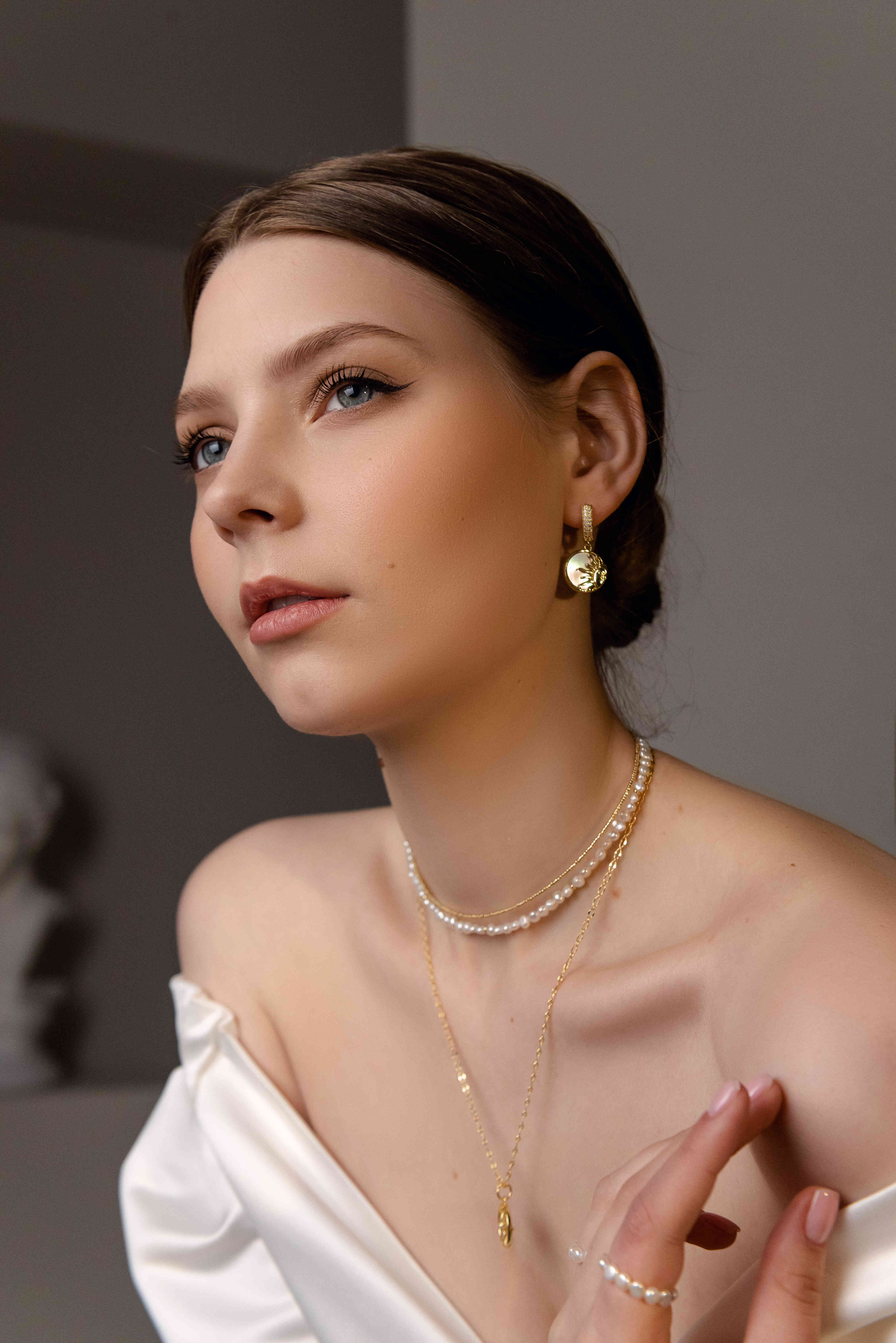 Woman wearing gold-plated jewelry including a necklace, earrings, and bracelet against a neutral background