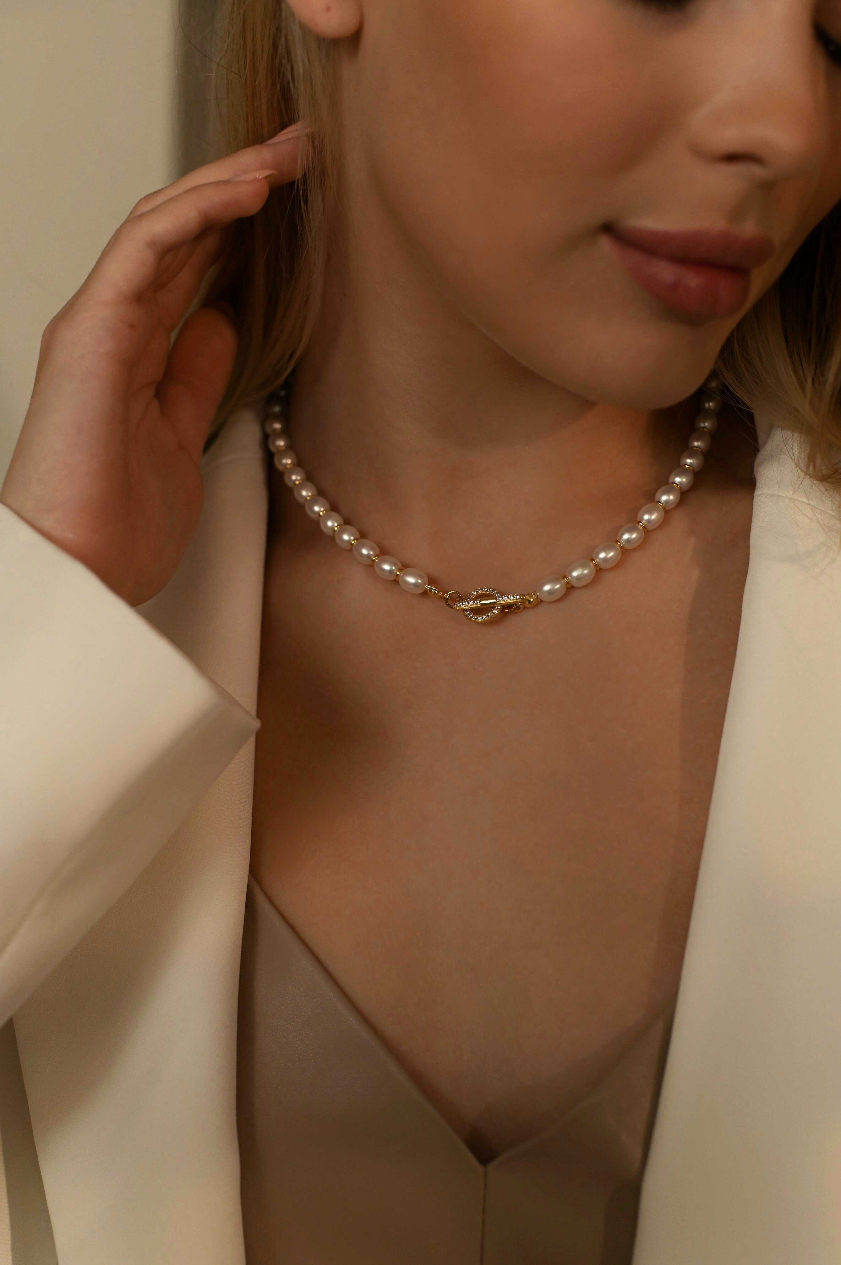 Woman wearing a pearl necklace with a gold-plated clasp, dressed in a white blazer and beige top.