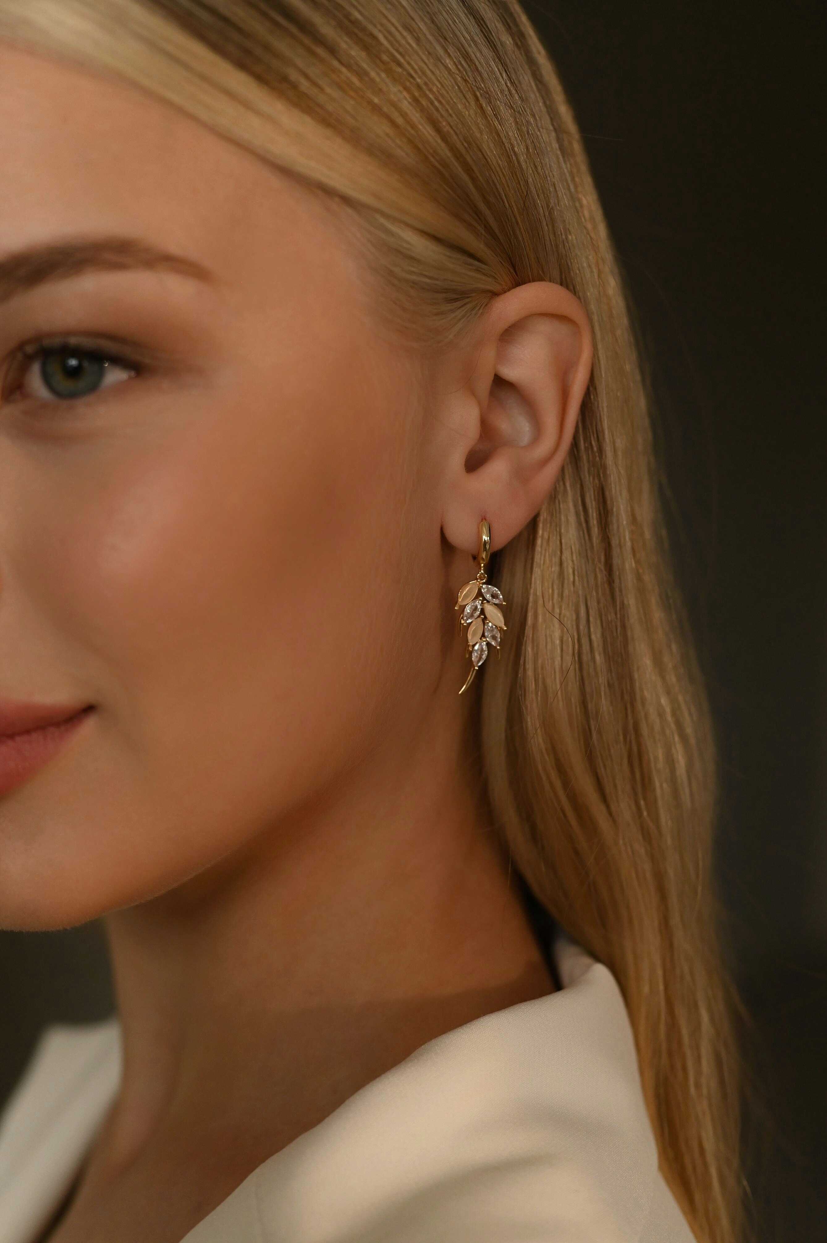 Close-up of a woman wearing a delicate leaf-shaped earring against a dark background