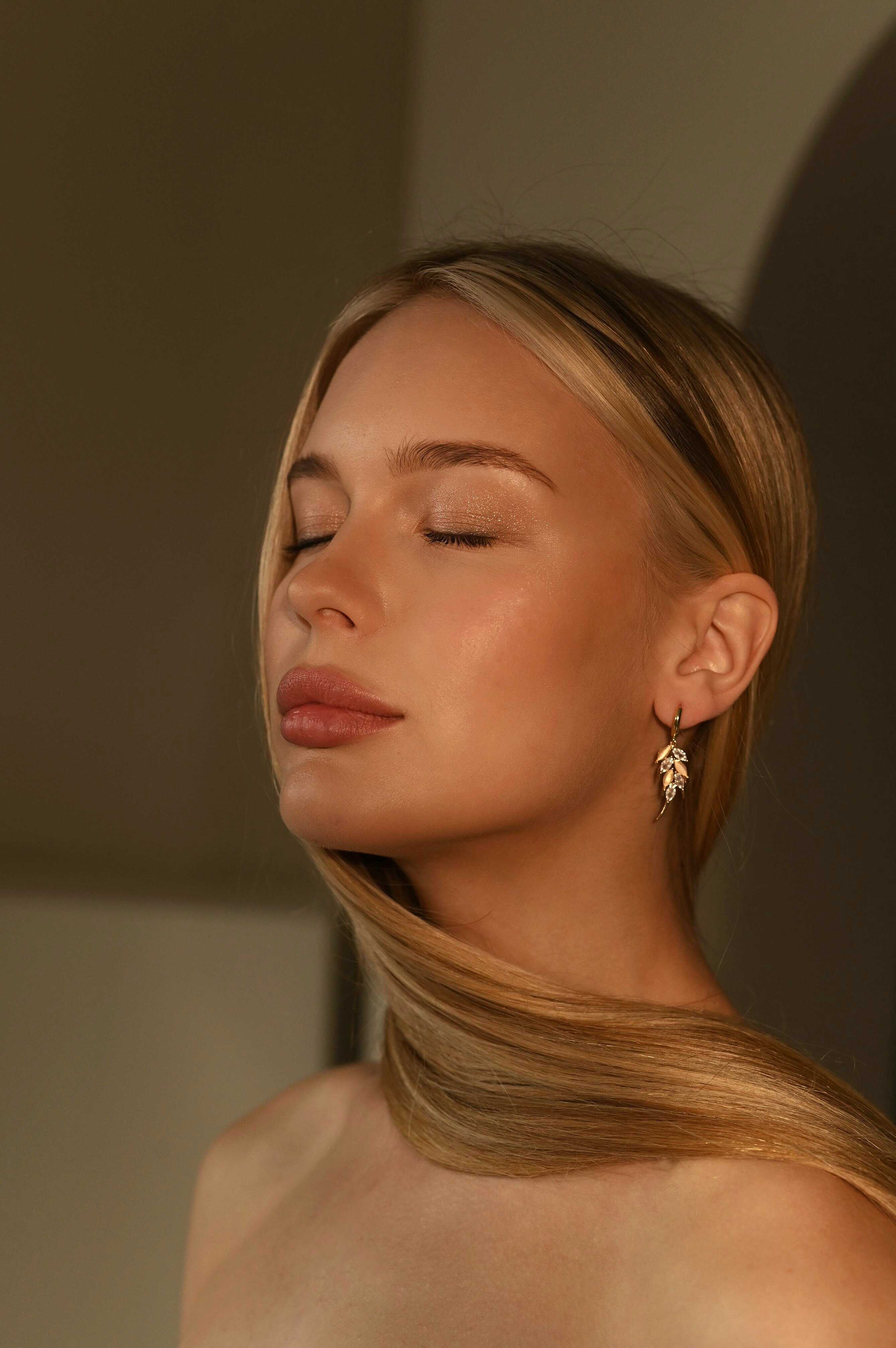 Woman with closed eyes wearing a delicate earring against a neutral background