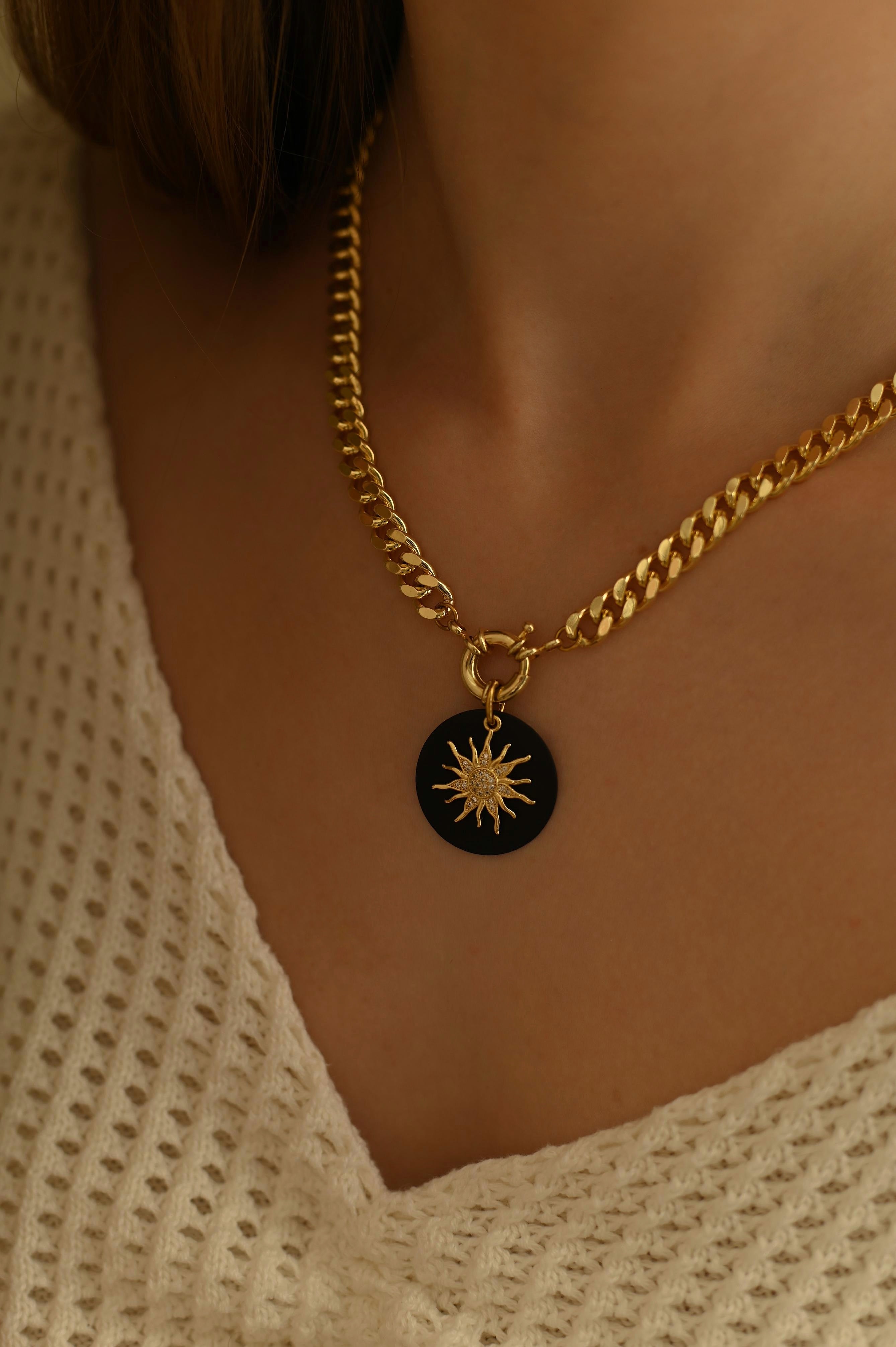 Bold gold-plated curb chain necklace with a detachable sun-shaped pendant adorned with sparkling cubic zirconia, offering versatile styling options.
