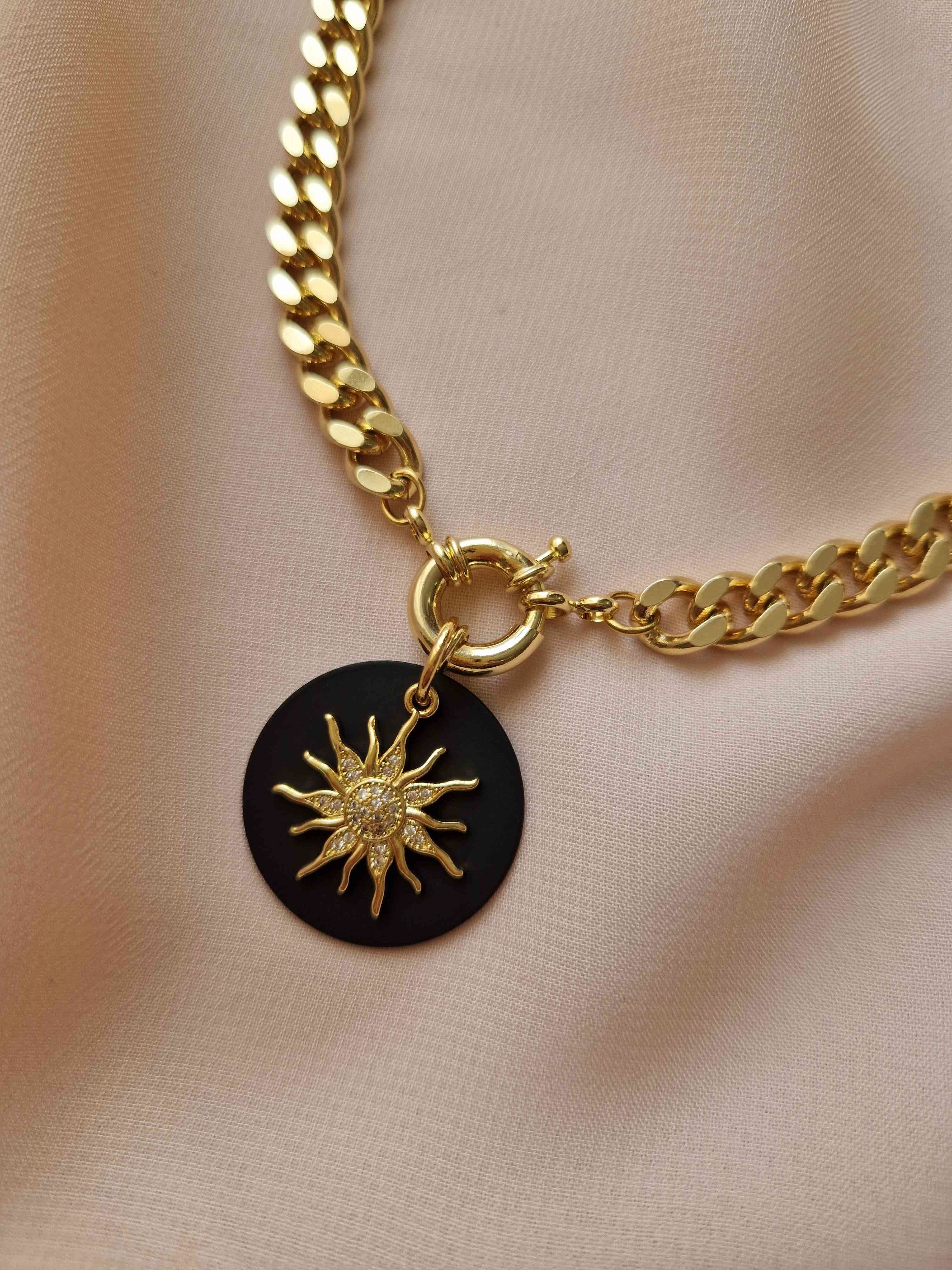 Gold-plated chain necklace with a sun pendant on a beige fabric background