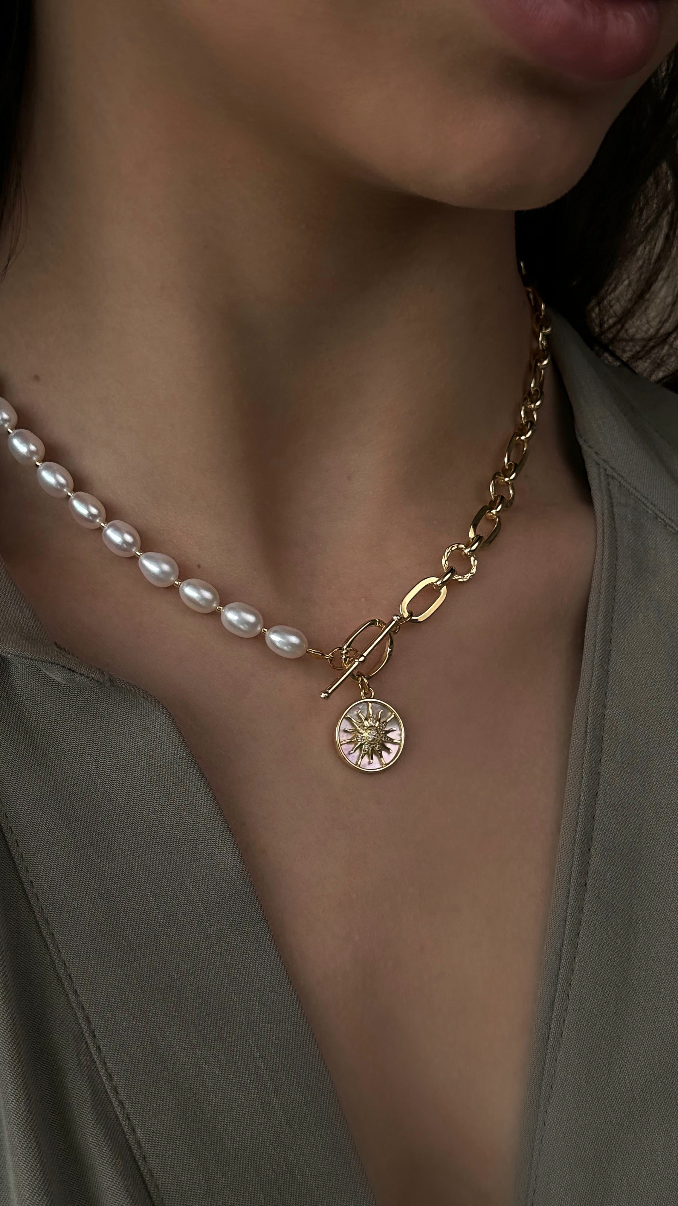 Gold-plated necklace with pearl beads and a round pendant worn by a person.