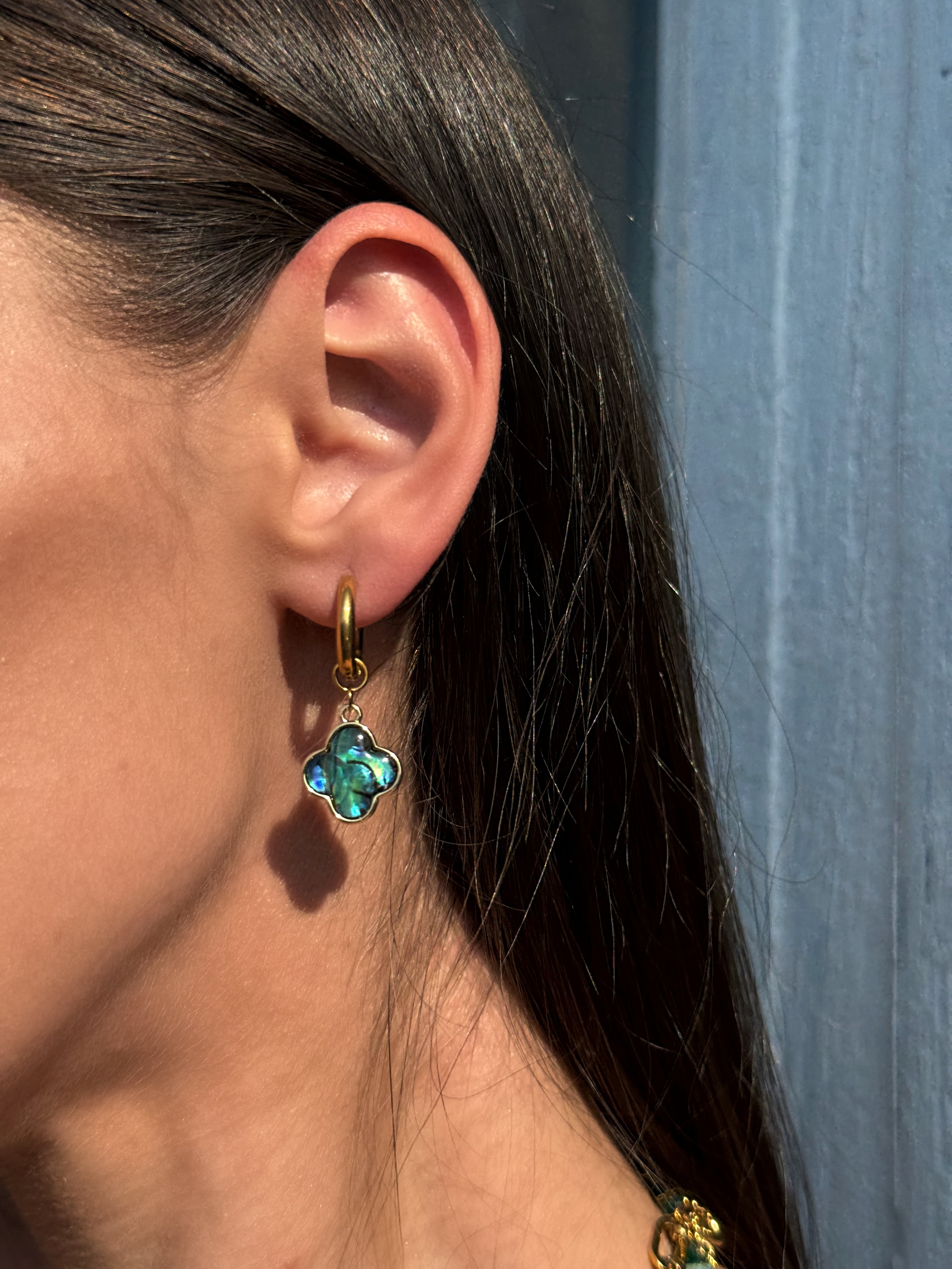 Close-up of an ear wearing a turquoise clover-shaped earring with a blurred blue background